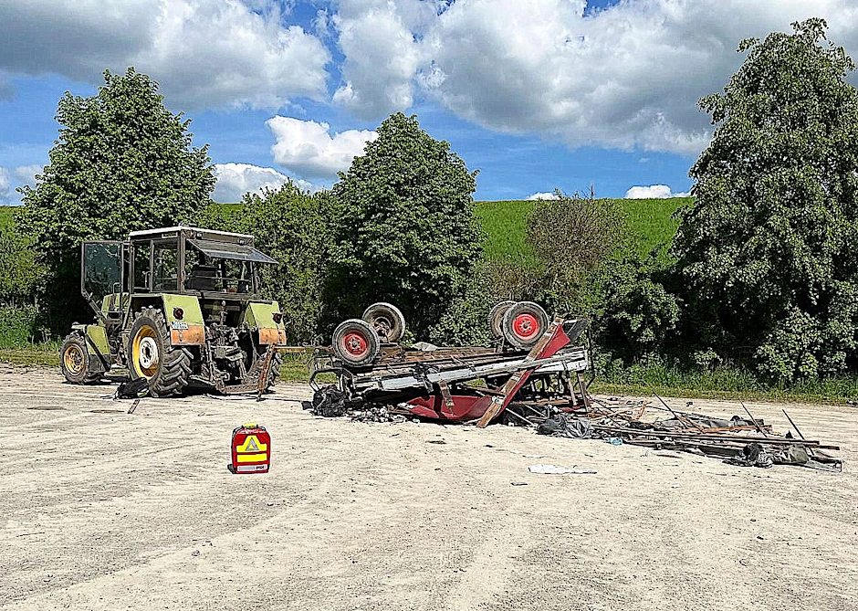 Ein umgestürzter Anhänger an einem Traktor liegt an der Unfallstelle.