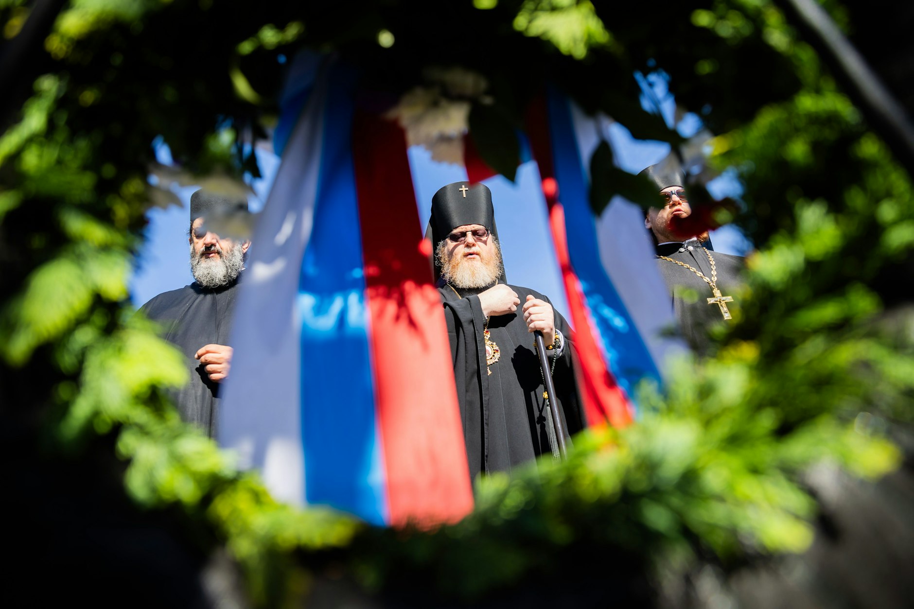 Russisch-orthodoxe Geistliche stehen am Sowjetischen Ehrenmal im Treptower Park vor einem Gedenkkranz mit russischer Flagge.