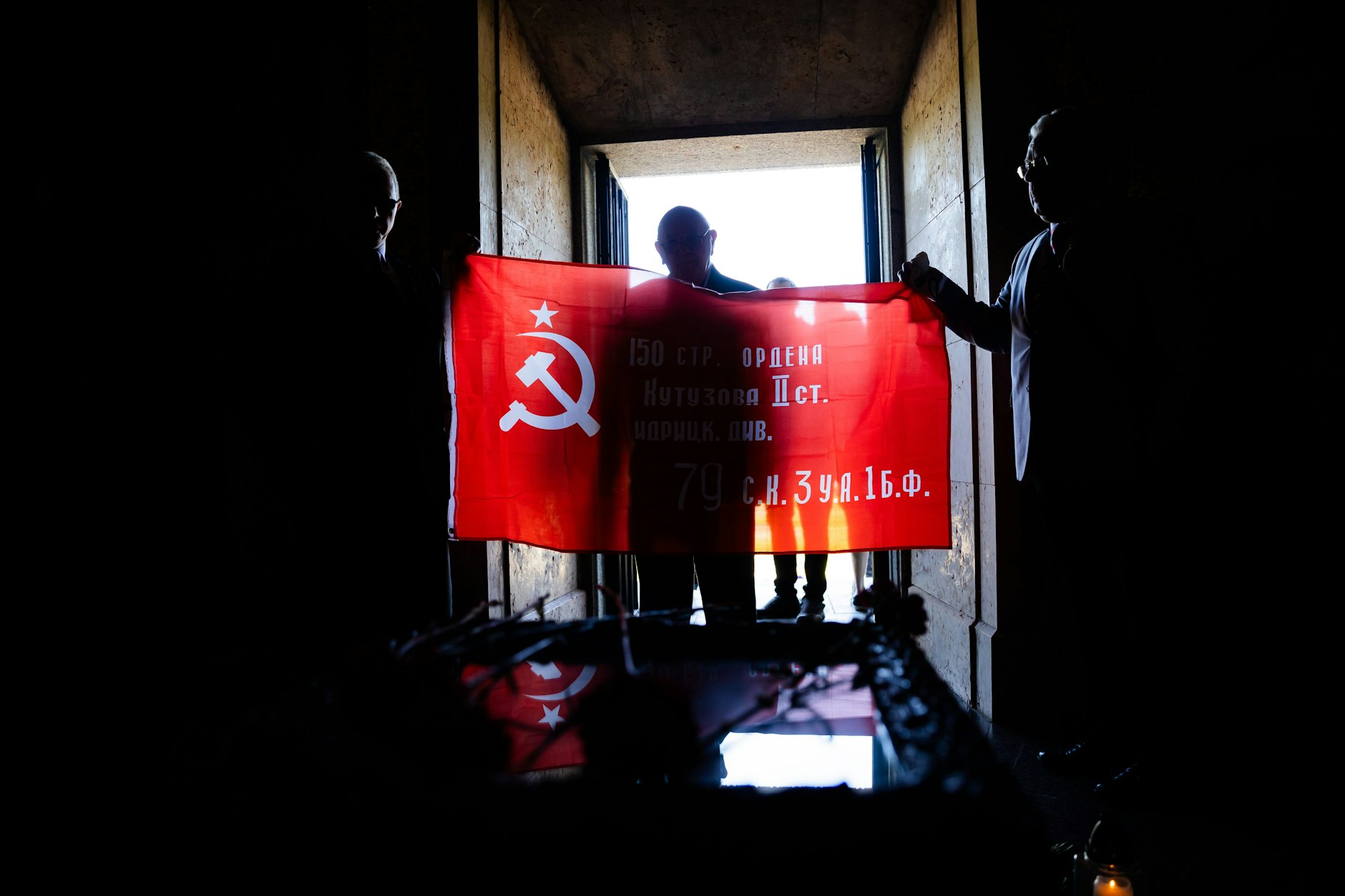 Am Sowjetischen Ehrenmal im Treptower Park halten Besucher eine Fahne mit Sichel und Hammer hoch.