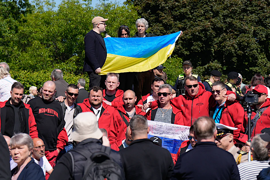 Stiller Protest: Drei Unterstützer der Ukraine strecken eine Flagge in die Höhe. Die russische Rocker-Gruppe Mayhem posiert demonstrativ mit einem russischen Pedant.