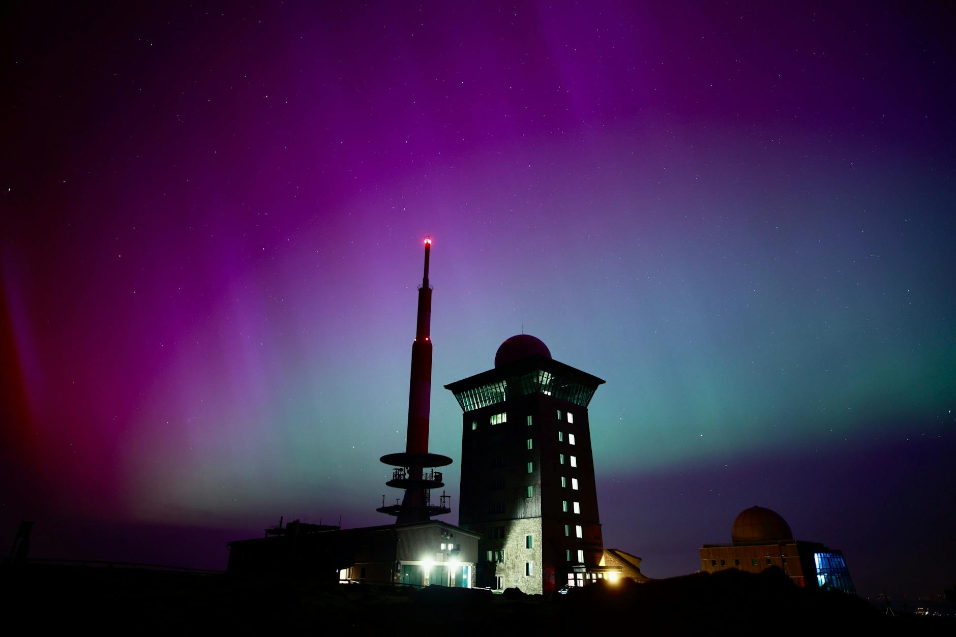 Polarlichter erscheinen über dem Brocken am Nachthimmel.