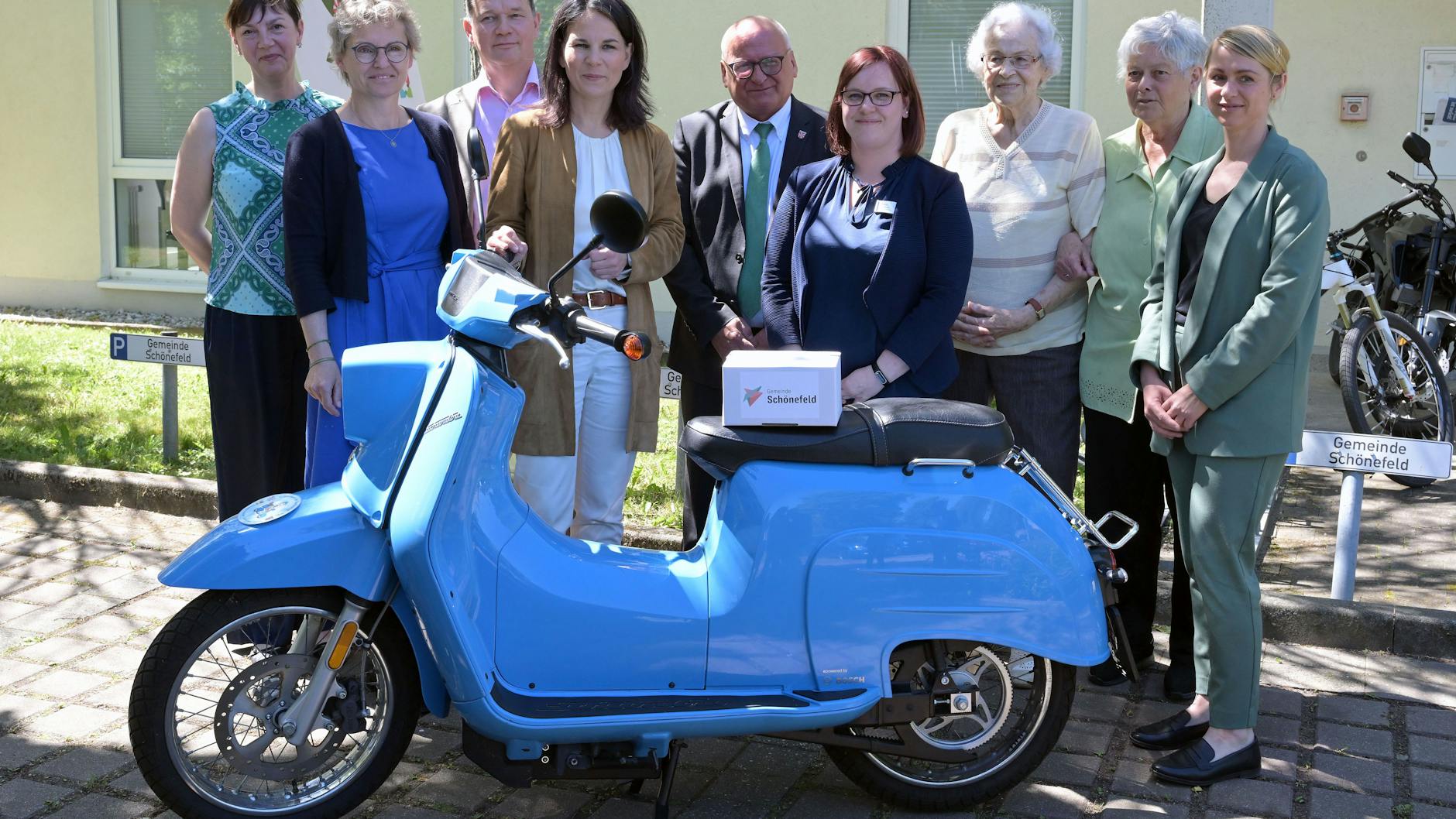 Bundestagsabgeordnete und Außenministerin Annalena Baerbock (Grüne) mit Akteuren des Projekt "Schwester Agnes" sowie Bewohnerinnen einer Seniorenunterkunft. Wie im Kultfilm ist man mit einem Moped unterwegs. 