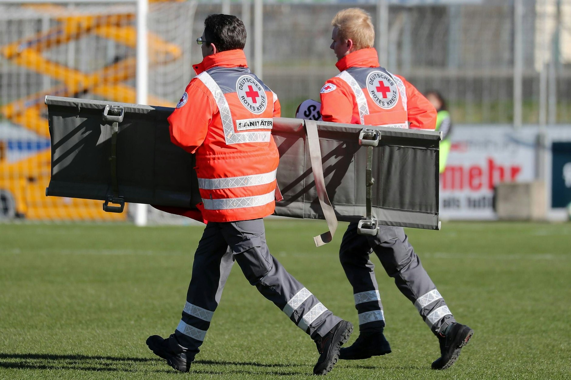 Zwei Sanitäter vom Roten Kreuz (Deutsches Rotes Kreuz, DRK) laufen mit einer Trage auf ein Spielfeld, Verletzung im Sportverletzung, Ersthelfer, Erste Hilfe, Verletzungspause, Symbolfoto, Symbolbild, Symbol, Fussball