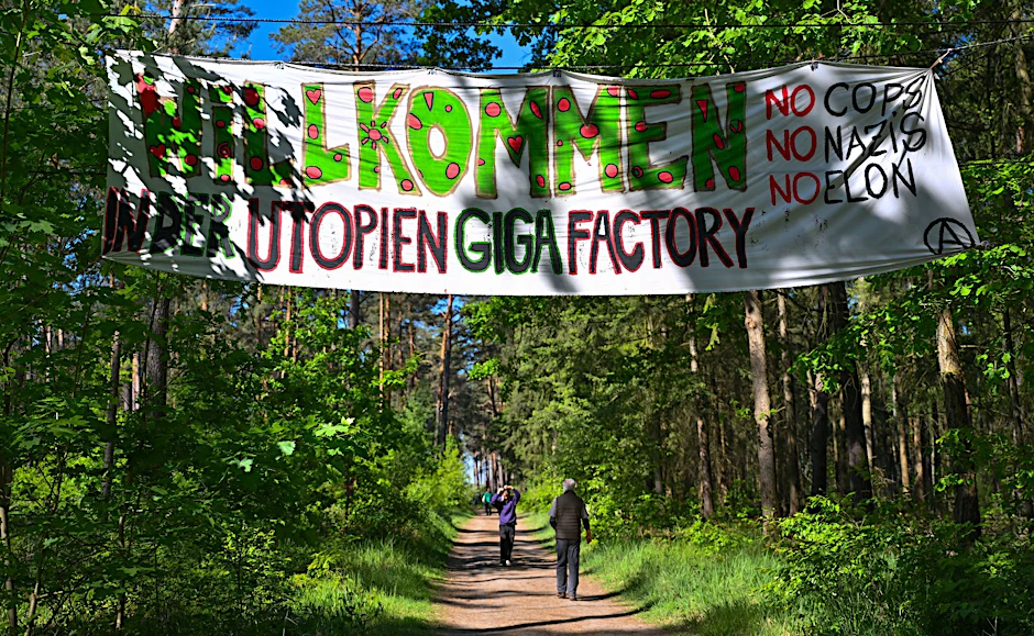 Aktivisten der Initiative «Tesla stoppen» haben in einem Wald nahe dem Werk der Tesla-Gigafactory Berlin-Brandenburg ein Transparent mit der Aufschrift «Willkommen in der Utopien Giga Factory No Cops, No Nazis, No Elon» aufgehängt.  