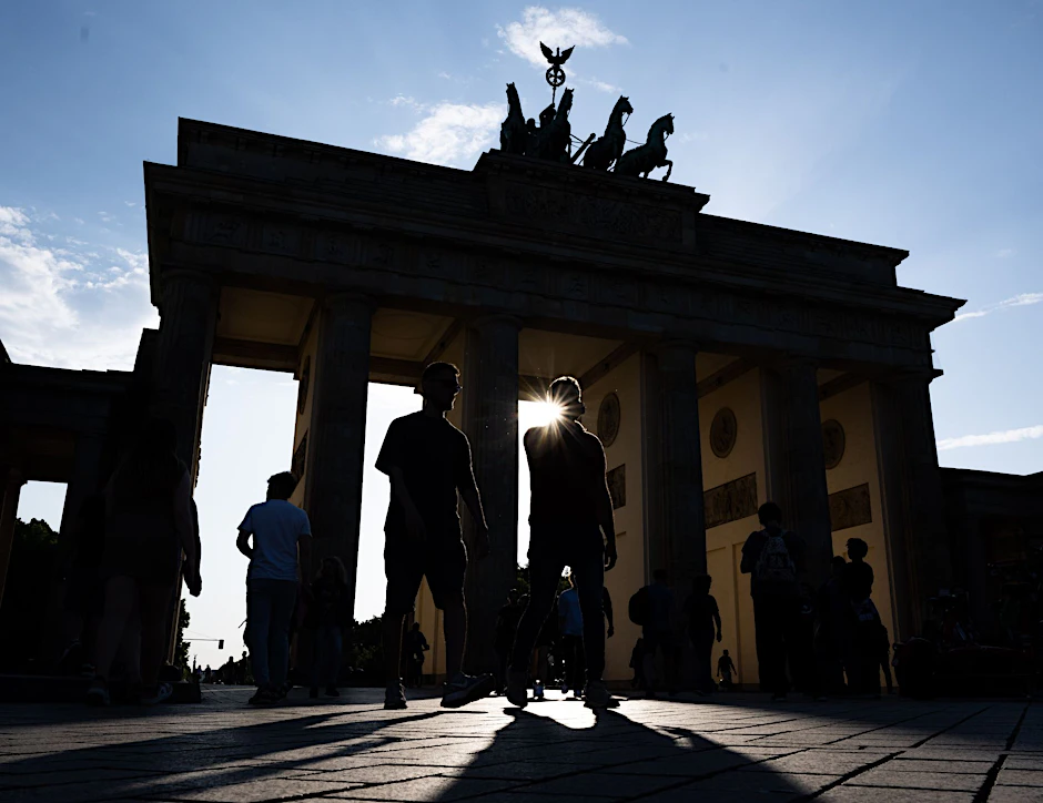 ARCHIV - Touristen gehen im Gegenlicht der untergehenden Sonne über den Pariser Platz vor der Kulisse vom Brandenburger Tor.  