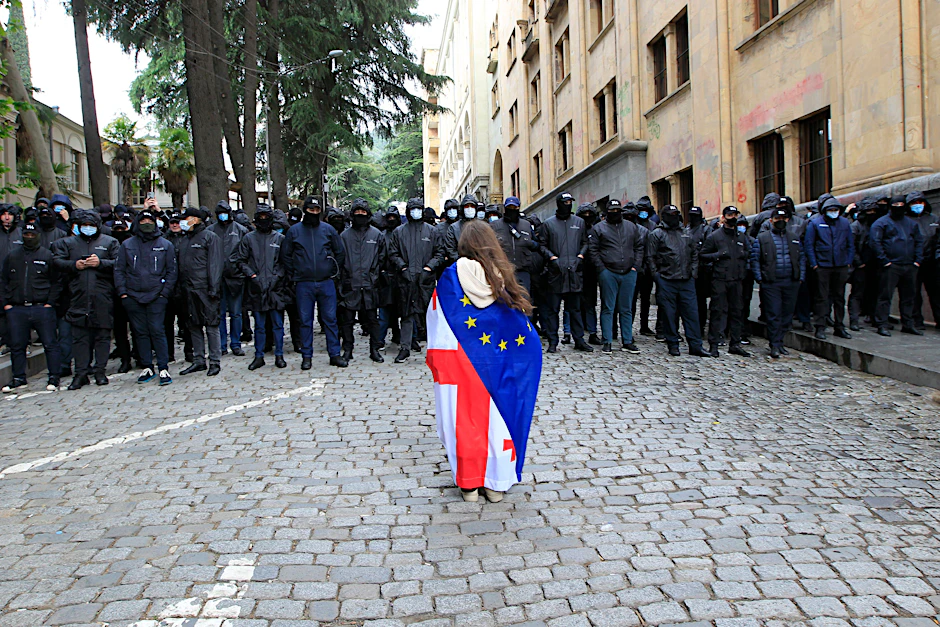 Eine Demonstrantin mit drapierter georgischer National- und EU-Flagge steht vor der Polizei, die den Weg zum Parlamentsgebäude blockiert.
