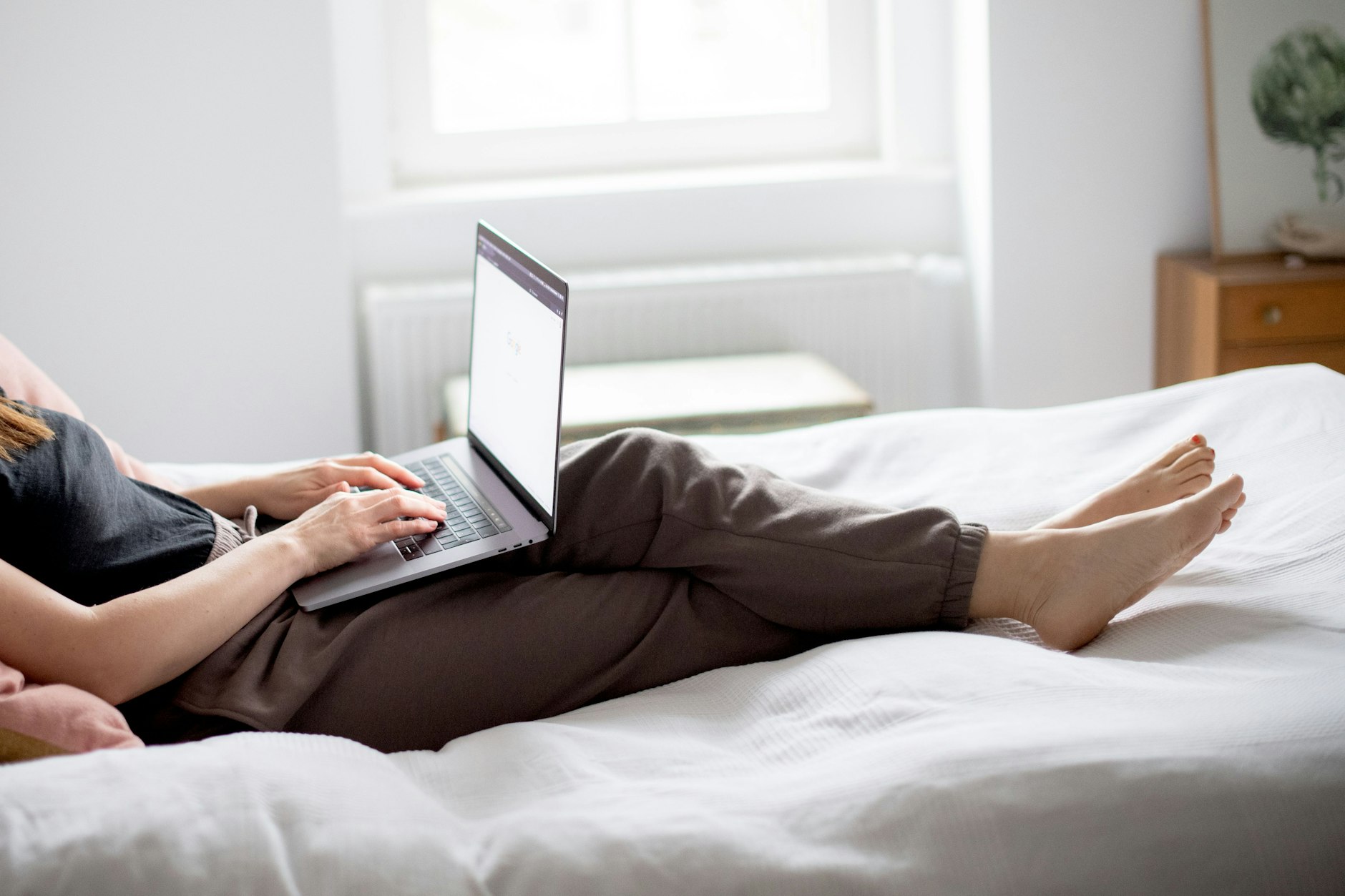 Eine Frau sitzt auf einem Bett und arbeitet mit ihrem Laptop.