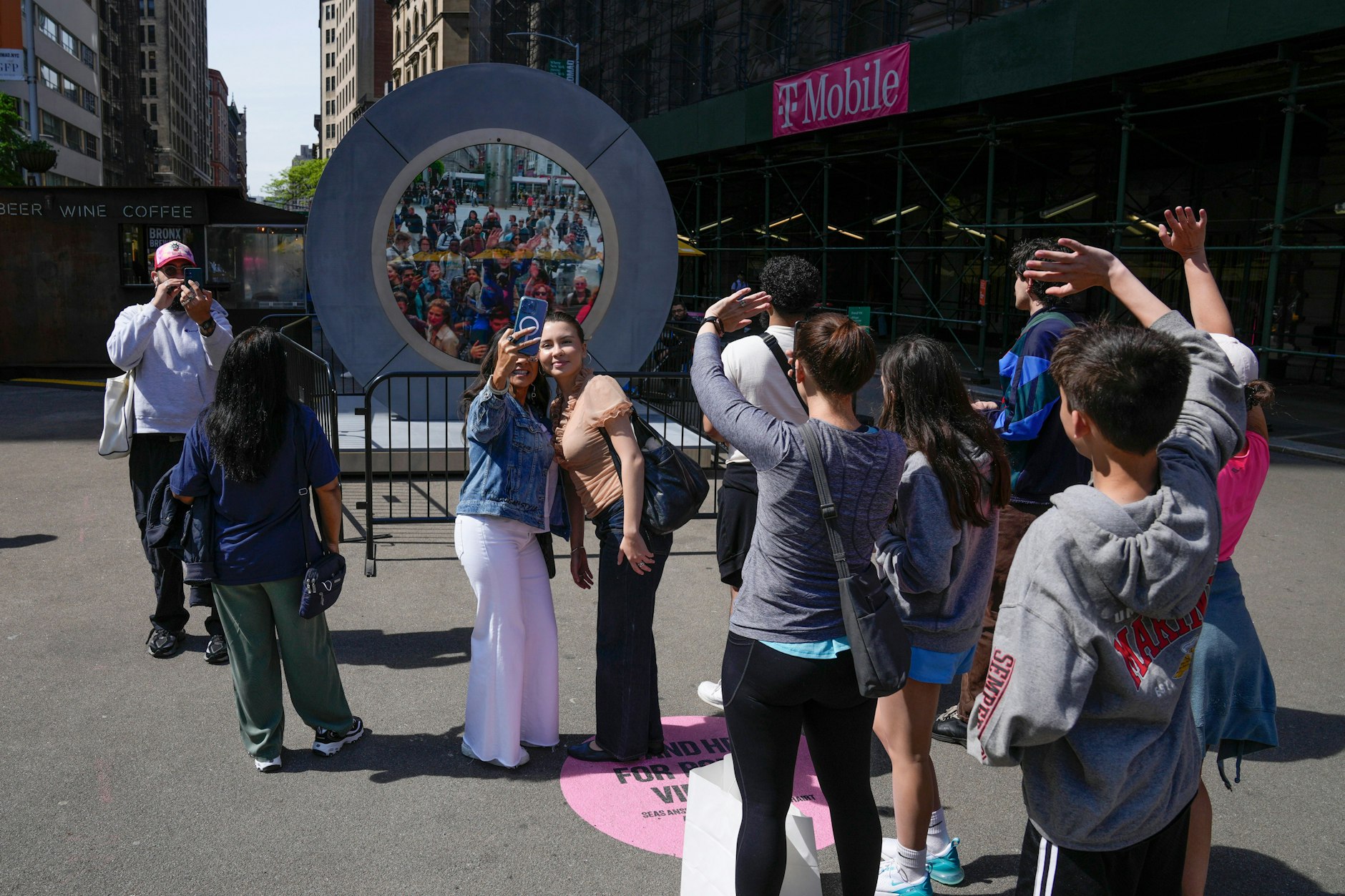 Menschen winken und machen Fotos, während sie eine per Livestream übertragene Ansicht von Dublin auf der Straße in New York betrachten.