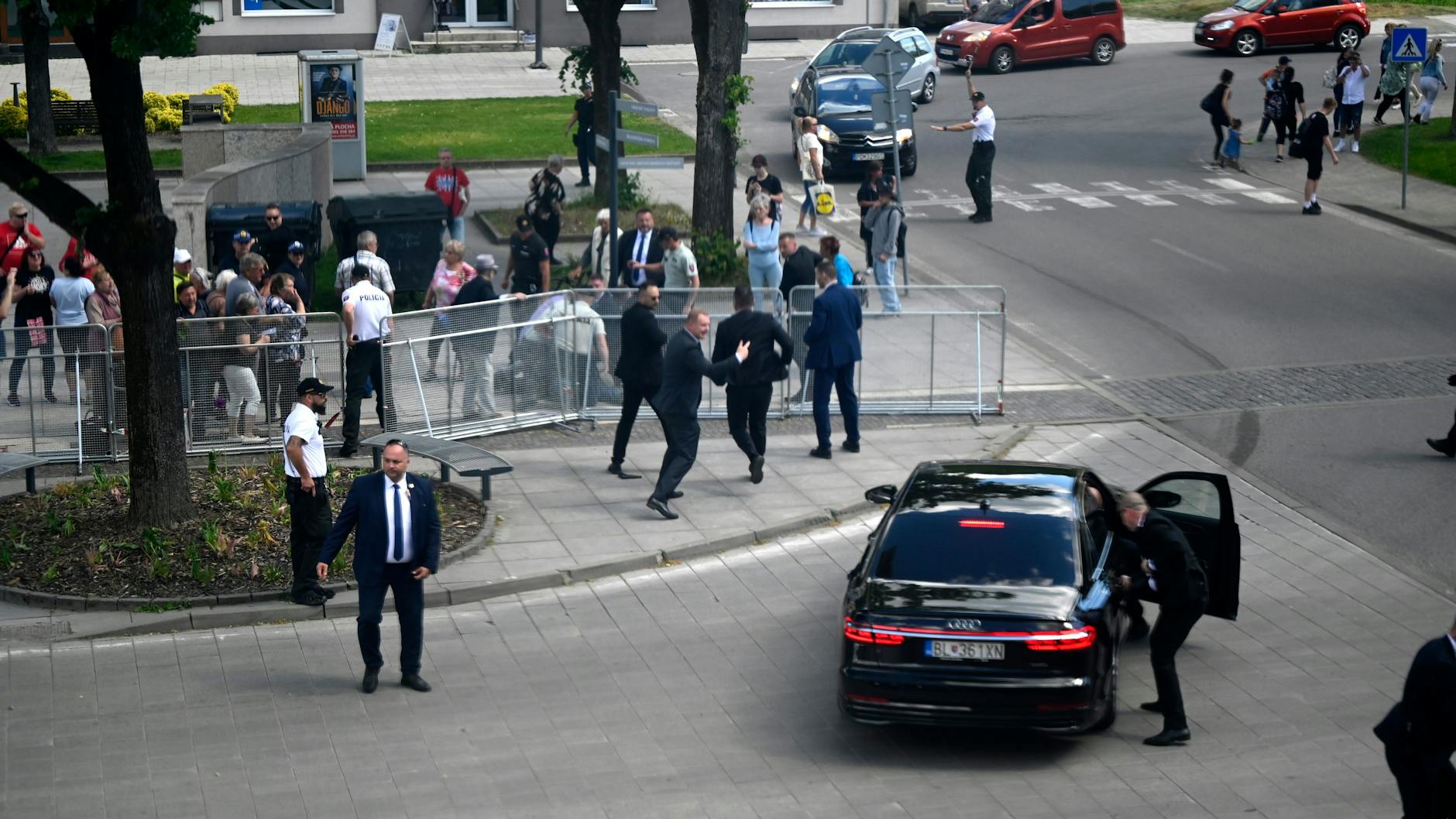 Leibwächter bringen Fico in einem Auto vom Ort des Geschehens in Sicherheit. Im Hintergrund wird der mutmaßliche Schütze festgenommen.