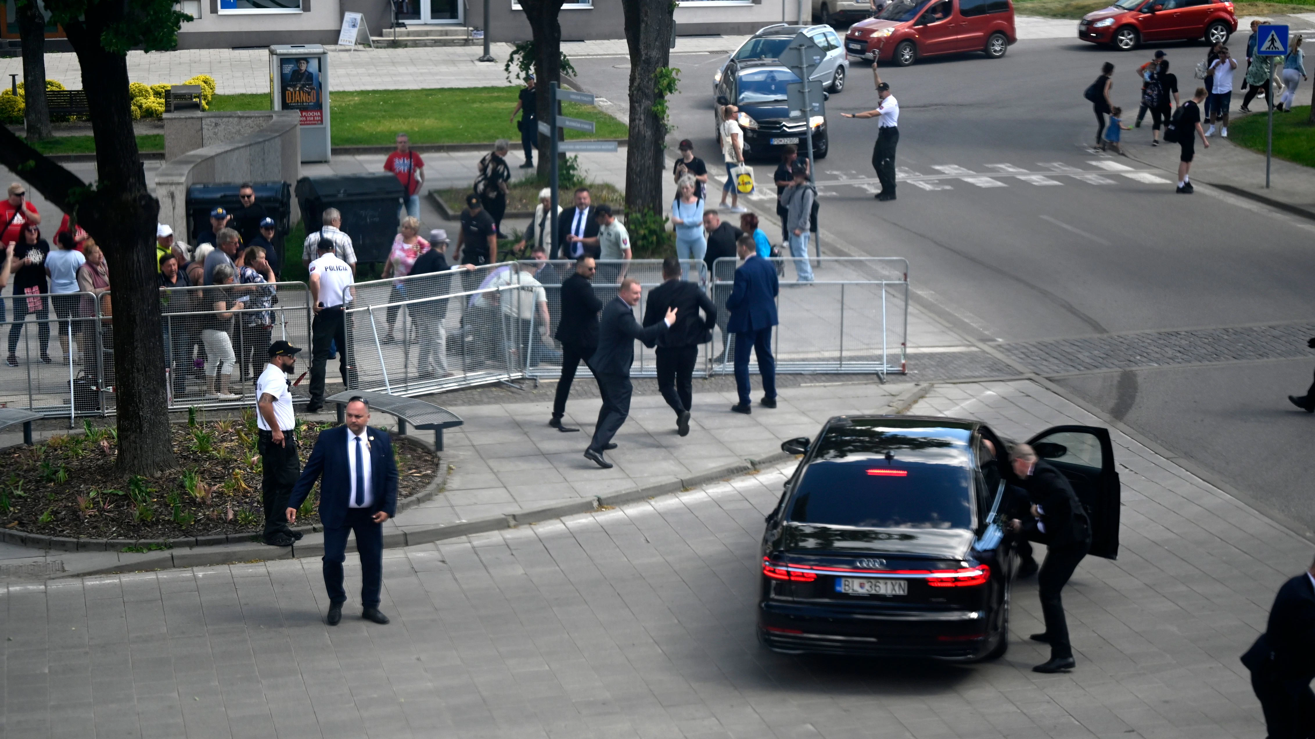 Leibwächter bringen Fico in einem Auto vom Ort des Geschehens in Sicherheit. Im Hintergrund wird der mutmaßliche Schütze festgenommen.