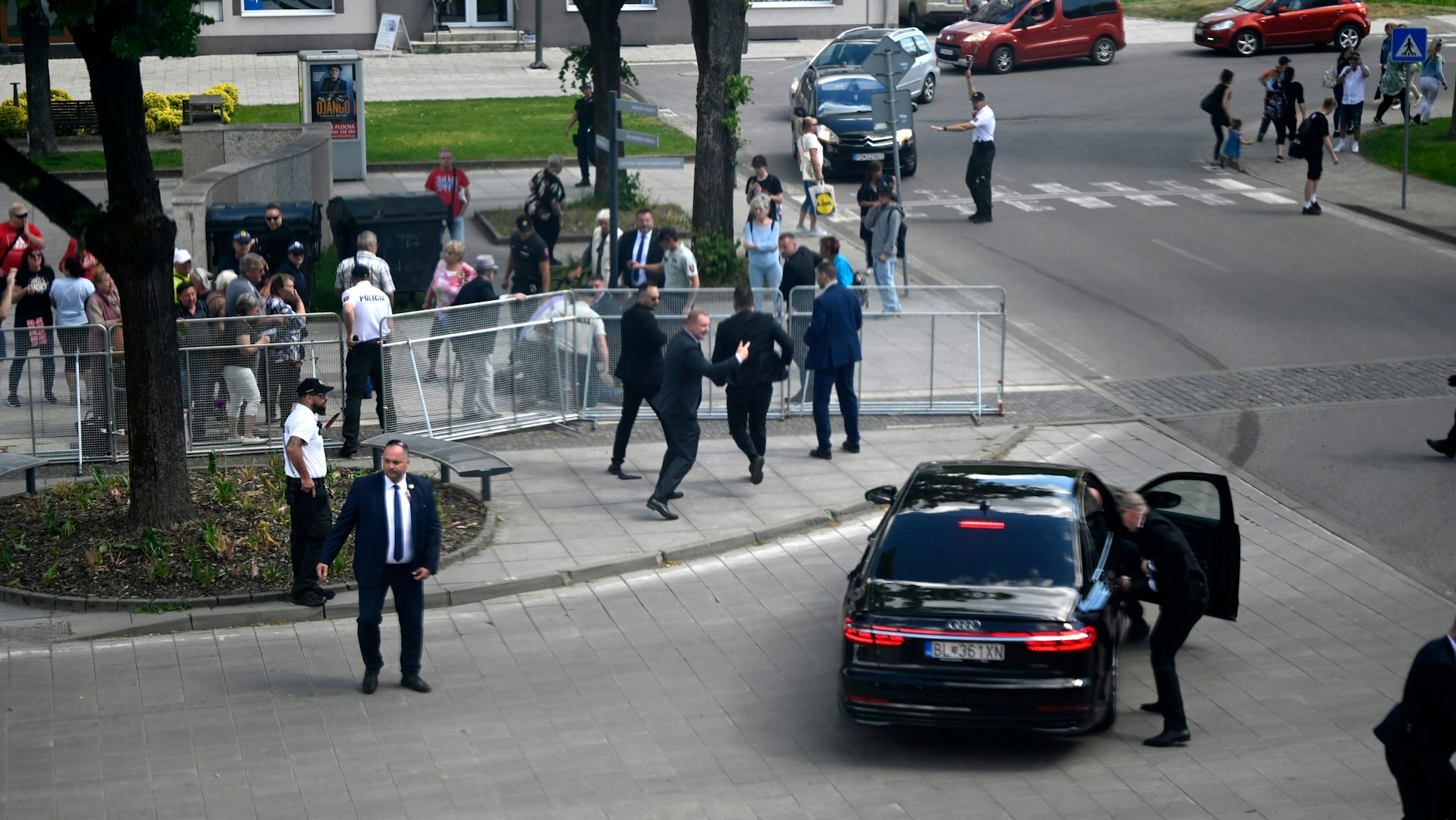 Leibwächter bringen Fico in einem Auto vom Ort des Geschehens in Sicherheit. Im Hintergrund wird der mutmaßliche Schütze festgenommen.