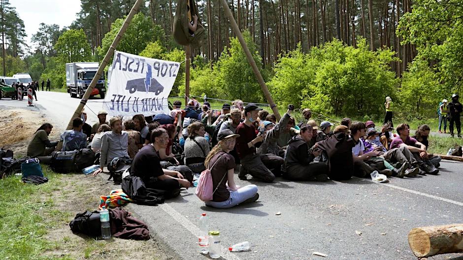 ARCHIV - Aktivisten blockieren bei einer Protestaktion gegen Tesla eine Straße. Aktivisten haben am Freitag versucht, auf das Werksgelände von Tesla in Grünheide vorzudringen.  