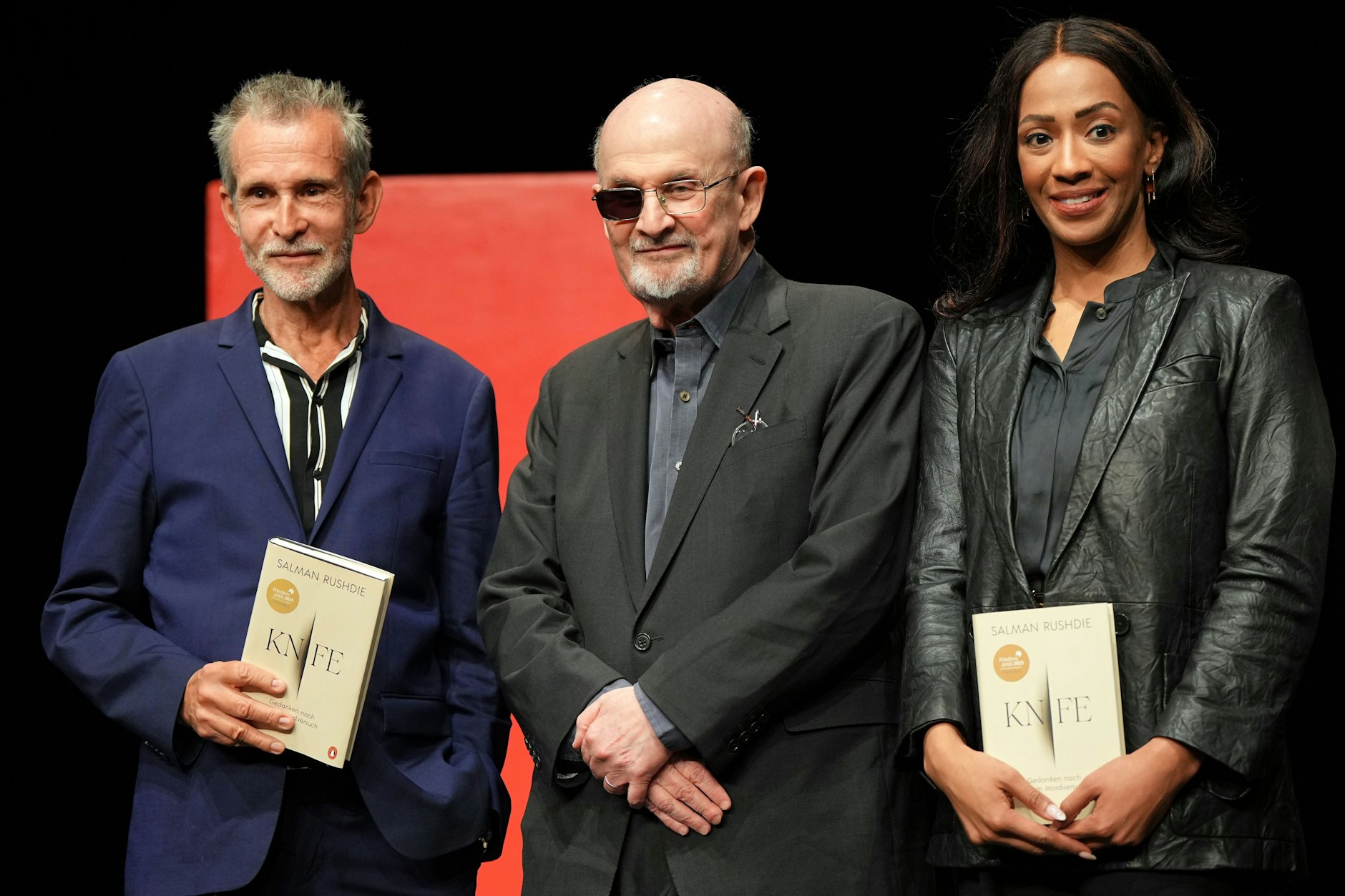 Der Schriftsteller Salman Rushdie (M), seine Ehefrau Rachel Eliza Griffiths (r) und der Schauspieler Ulrich Matthes (l), im Deutschen Theater bei der deutschen Buchpremiere von „Knife. Gedanken nach einem Mordversuch“