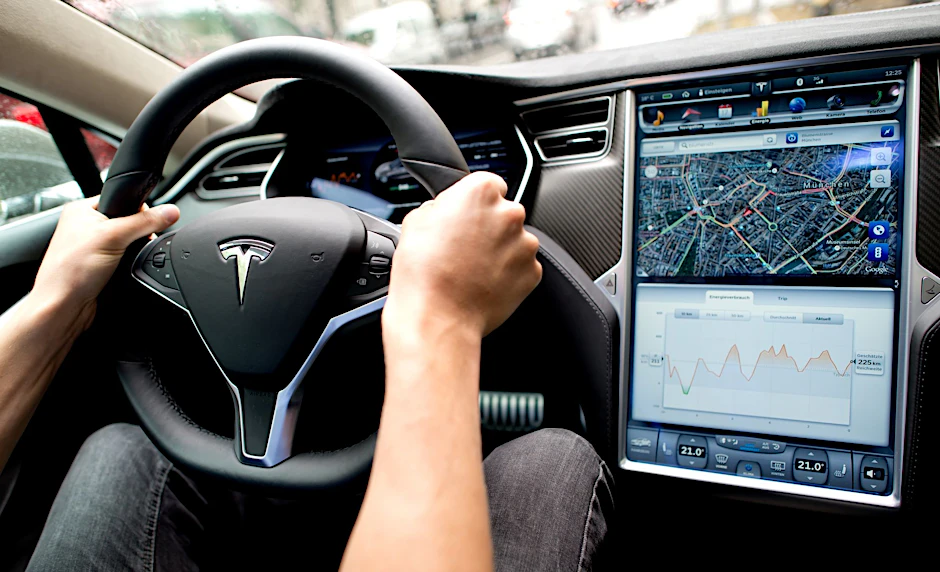 ARCHIV - Ein Mann sitzt in einem Tesla Model S am Lenkrad: Elon Musk sagt, er sei mit seinen Versprechen zu selbstfahrenden Autos oft zu optimistisch gewesen.  