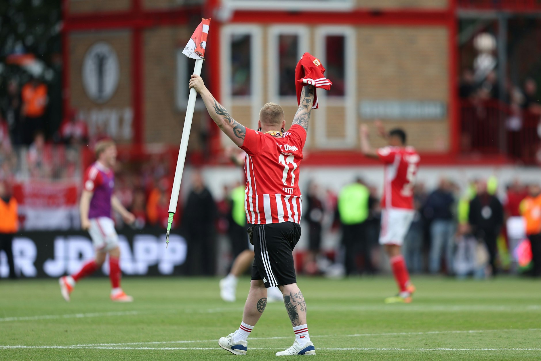 Ein Fan des 1. FC Union Berlin hat sich eine Eckfahne geschnappt und läuft jubelnd über den Rasen.