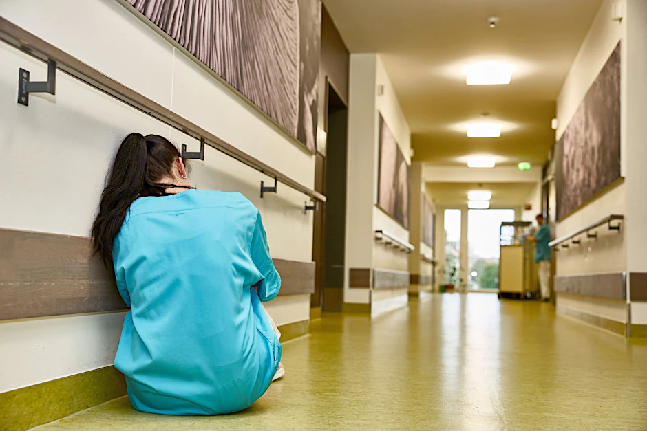 Eine erschöpfte Mitarbeiterin kauert im Flur eines Pflegeheims. Beschäftigte im Gesundheitssektor sind oft von Burnout betroffen.