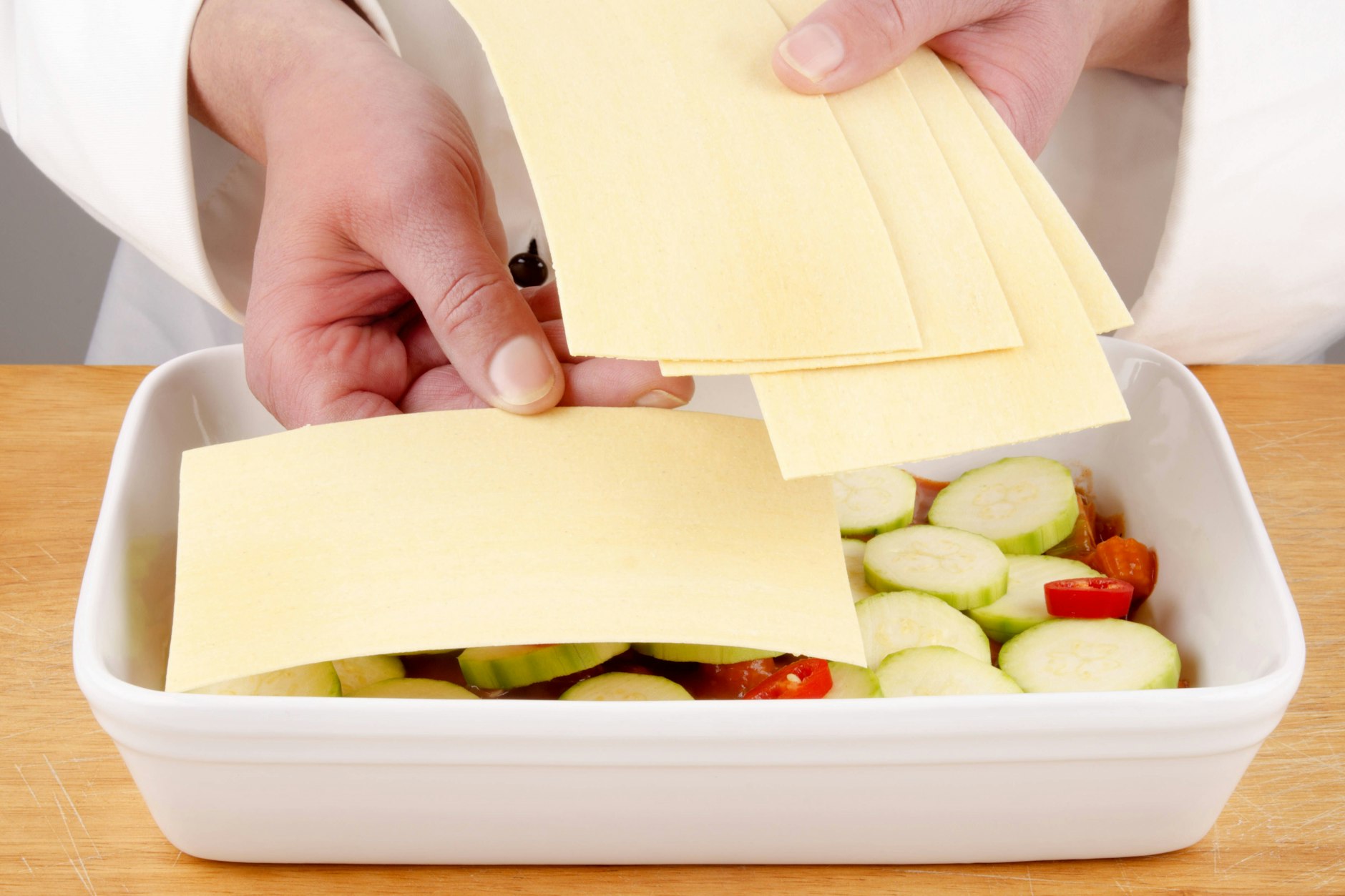 Rezept für Gemüselasagne: Schichtweise Zusammenstellung der Lasagne in einer Auflaufform –Lasagneblätter, Gemüsesoße, Béchamelsoße und Käse. Schichten Sie die Lasagne sorgfältig, um eine perfekte Balance aus Gemüse, Soße und Käse zu erreichen.