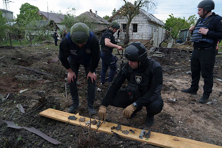 Ein ukrainischer Polizeibeamter und ein Staatsanwalt für Kriegsverbrechen inspizieren Bruchstücke einer Gleitbombe vor einem beschädigten Haus nach einem russischen Luftangriff auf ein Wohnviertel.  