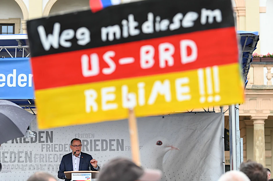 ARCHIV - Ein antiamerikanisches Plakat auf einer AfD-Kundgebung mit Bundessprecher Tino Chrupalla in Magdeburg (Archivbild).  