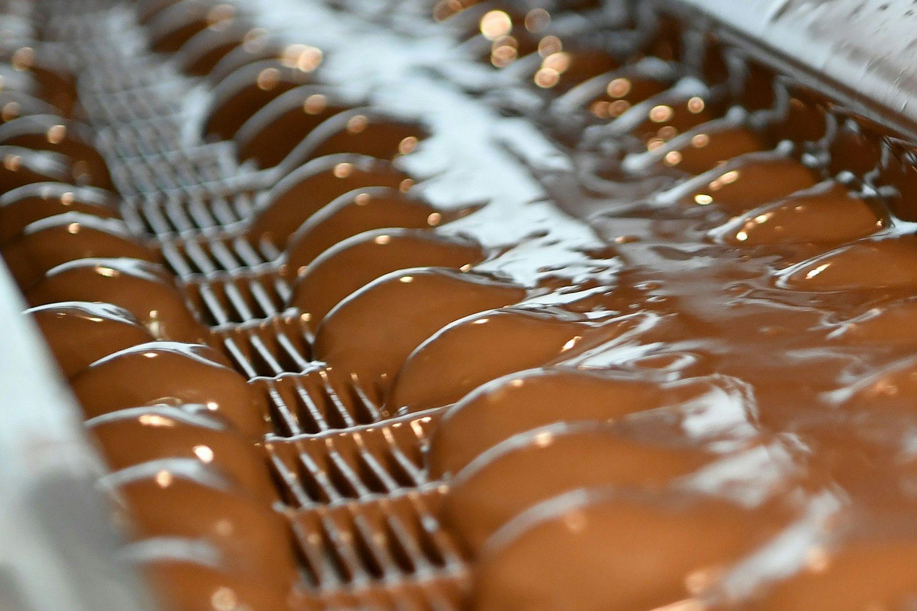 Schokoherzen werden an einer Fertigungslinie mit Schokolade übergossen.