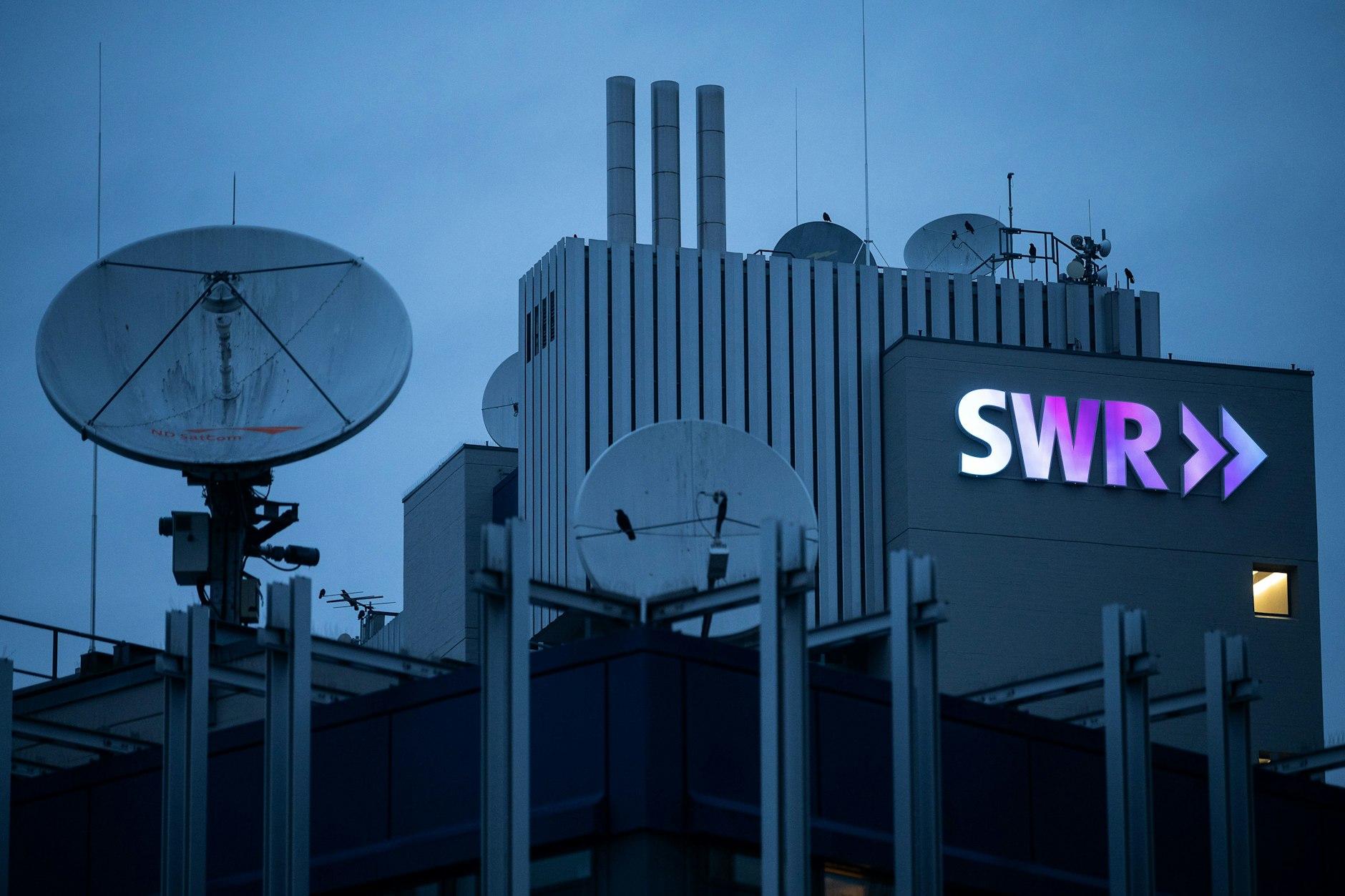 Das Logo des Südwestrundfunks (SWR) leuchtet am frühen Morgen am Funkhaus.