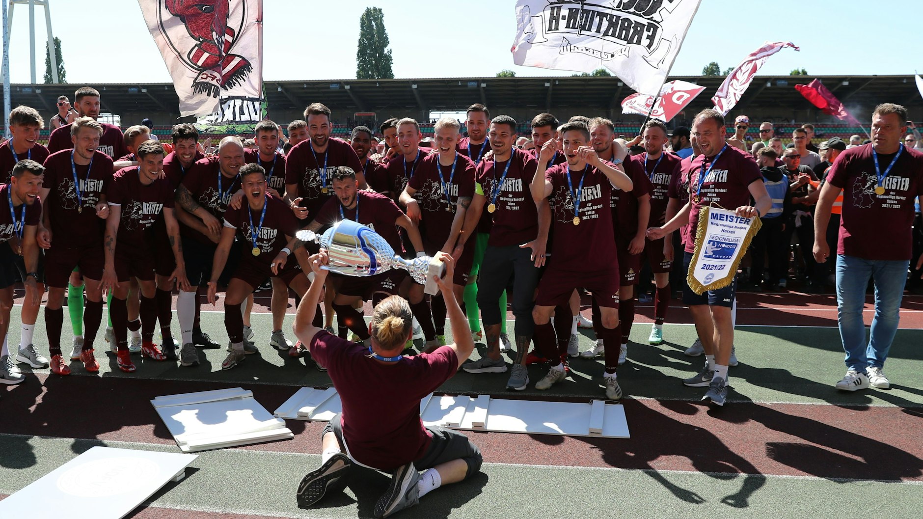 Mitte Mai 2022 feiert der BFC Dynamo den Meistertitel, Kevin Sommer jubelt den Kollegen auf Knien mit der Trophäe zu.