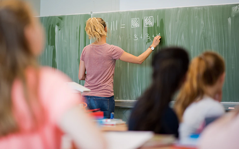 Eine junge Lehrerin schreibt im Mathematikunterricht an eine Schultafel.&nbsp;
