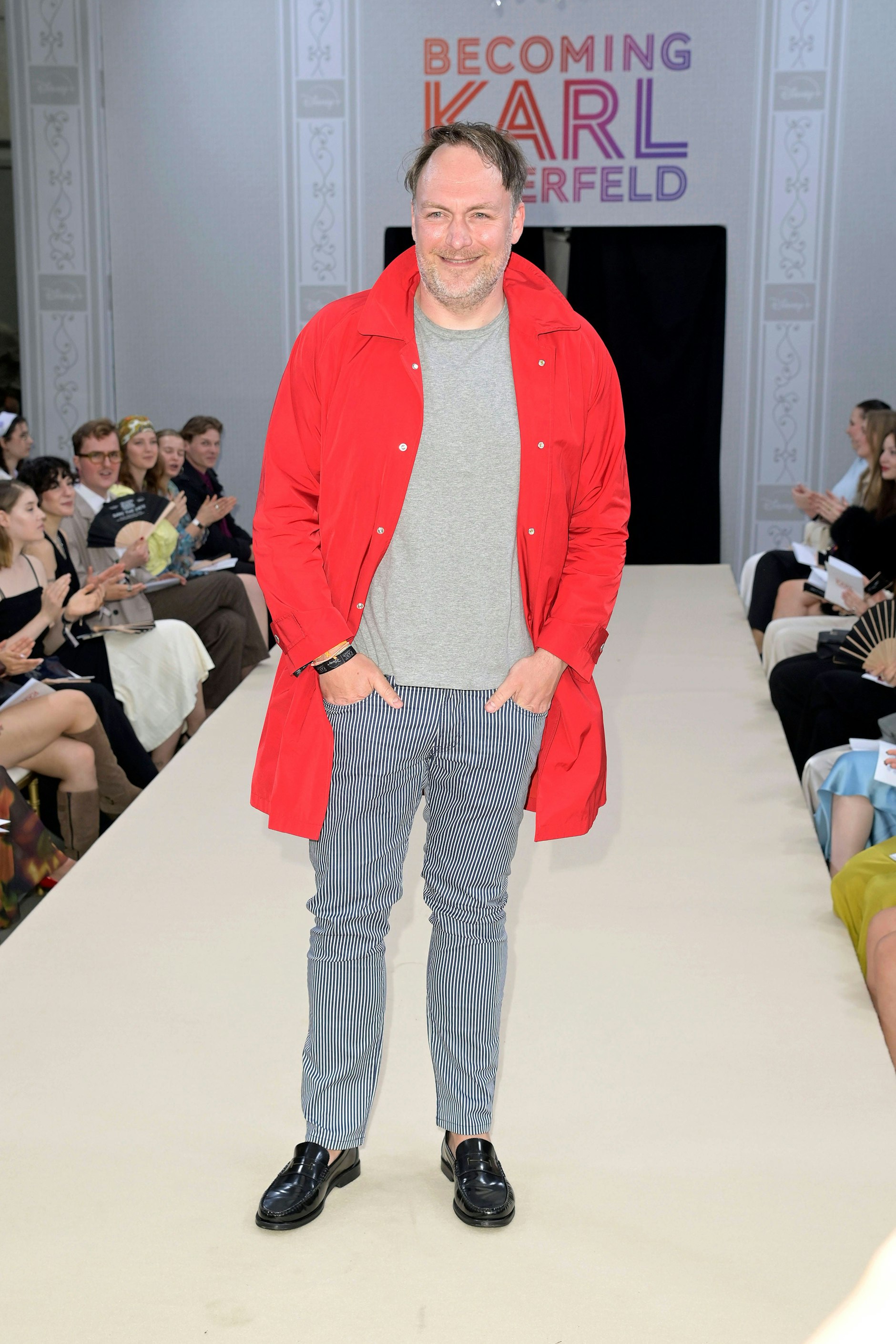 <strong>FLOP:</strong> Für dieses Premierenoutfit kann es nur eine Erklärung geben. Der Schauspieler <strong>Martin Stange</strong>, bekannt unter anderem aus der Serie „Gute Zeiten, schlechte Zeiten“, war nur zufällig in der Nähe. Er kam gerade vom Einkauf im Hit-Ullrich-Verbrauchermarkt am Zoo und war auf dem Heimweg, als er die vielen Menschen vor dem Kino sah. Mensch, dachte er sich, da schau ich doch mal rein und laufe über den Catwalk. Egal, dass mein zusammengewürfeltes Outfit eigentlich wenig vorzeigbar ist, in Berlin, da geht das schon! Immerhin, das muss man Stange lassen, man kann am Beispiel seiner Hose sehr gut verdeutlichen, was man auf keinen Fall tragen sollte, wenn man vor die Kamera tritt. Nämlich karierte Stoffe, Muster wie Streifen, Pepita, Fischgrät, kleine Punkte und feine Linien. Sollten Sie diese Regel missachten, passiert das, was wir hier sehen: Sie sehen aus wie eines dieser Magic-Eye-Bilder aus den Neunzigern, bei deren längerem Betrachten sich plötzlich 3D-Objekte herauslösen.