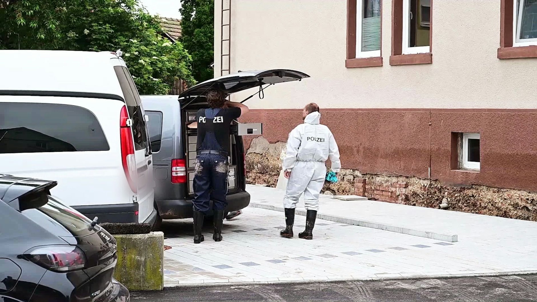 Schorndorf in Baden-Württemberg: Polizeibeamte der Spurensicherung stehen an ihrem Auto im Stadtteil Miedelsbach. Sie untersuchen einen Fundort der beiden Leichen, die nach einem Unwetter in einem Keller gefunden worden waren.