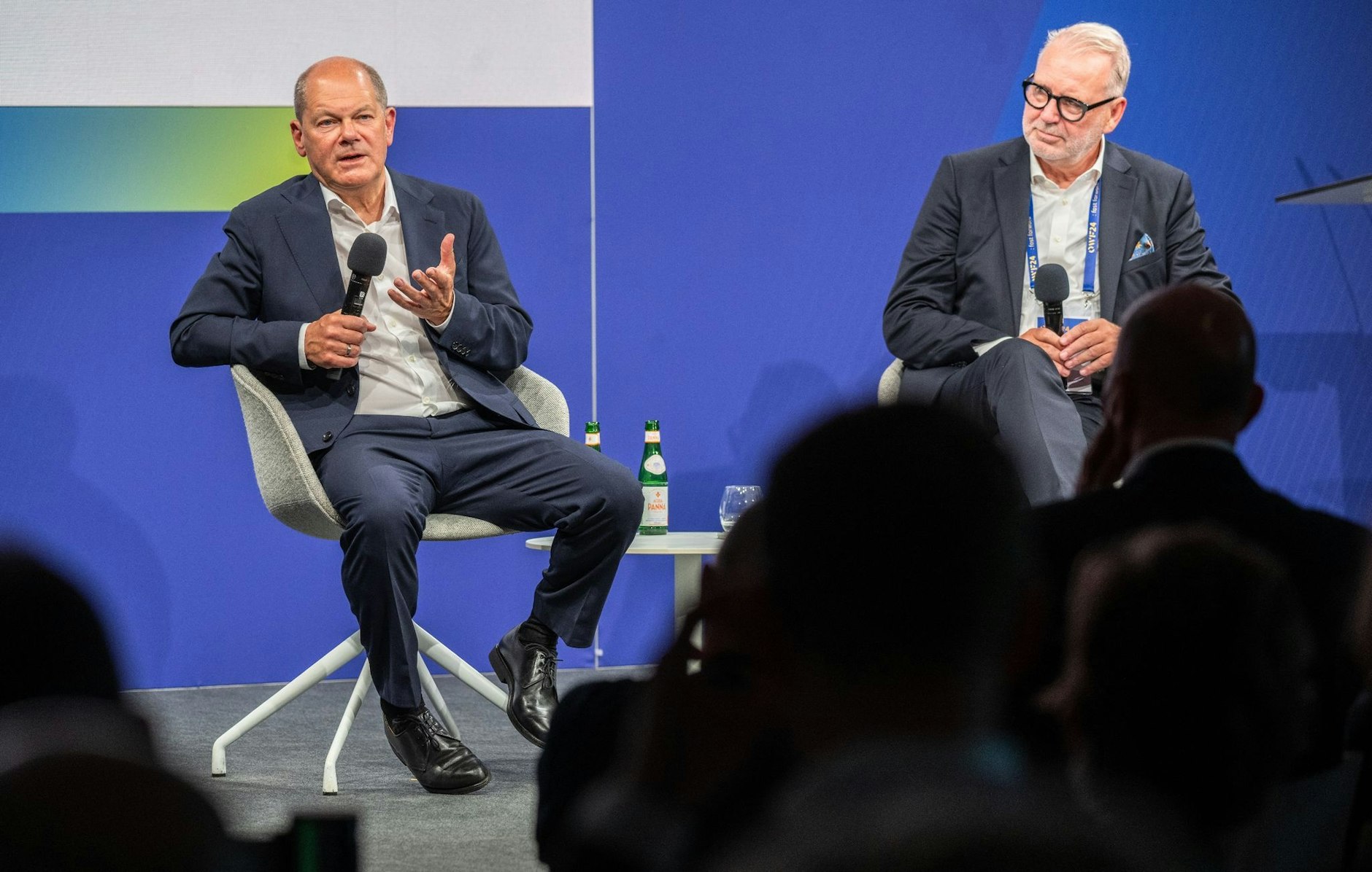 Bundeskanzler Olaf Scholz (l, SPD) und Frank Nehring, Präsident Ostdeutsches Wirtschaftsforum (OWF) sitzen beim Ostdeutschen Wirtschaftsforum im Theater am See auf der Bühne.  