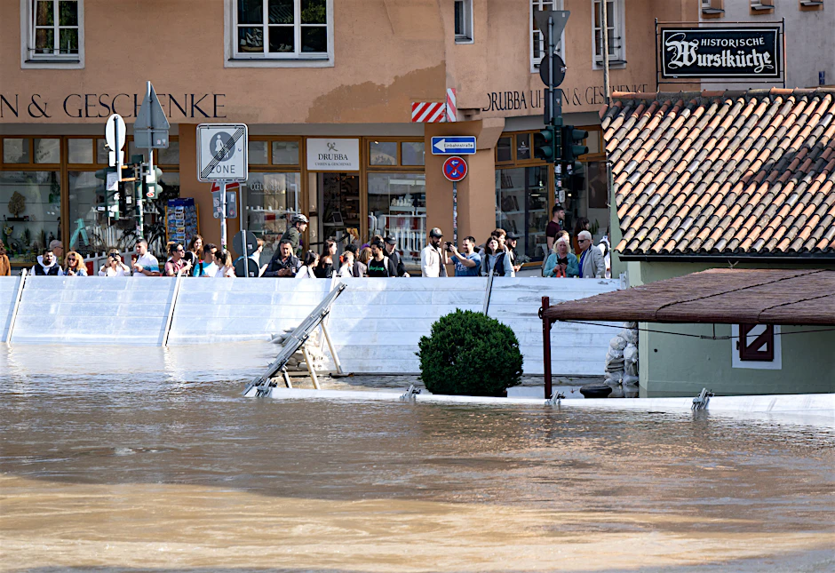 Menschen schauen sich in der Regensburger Altstadt am Donauufer hinter einer Schutzwand das Hochwasser an. Seit Mittwoch sinken die Pegel langsam.&nbsp;