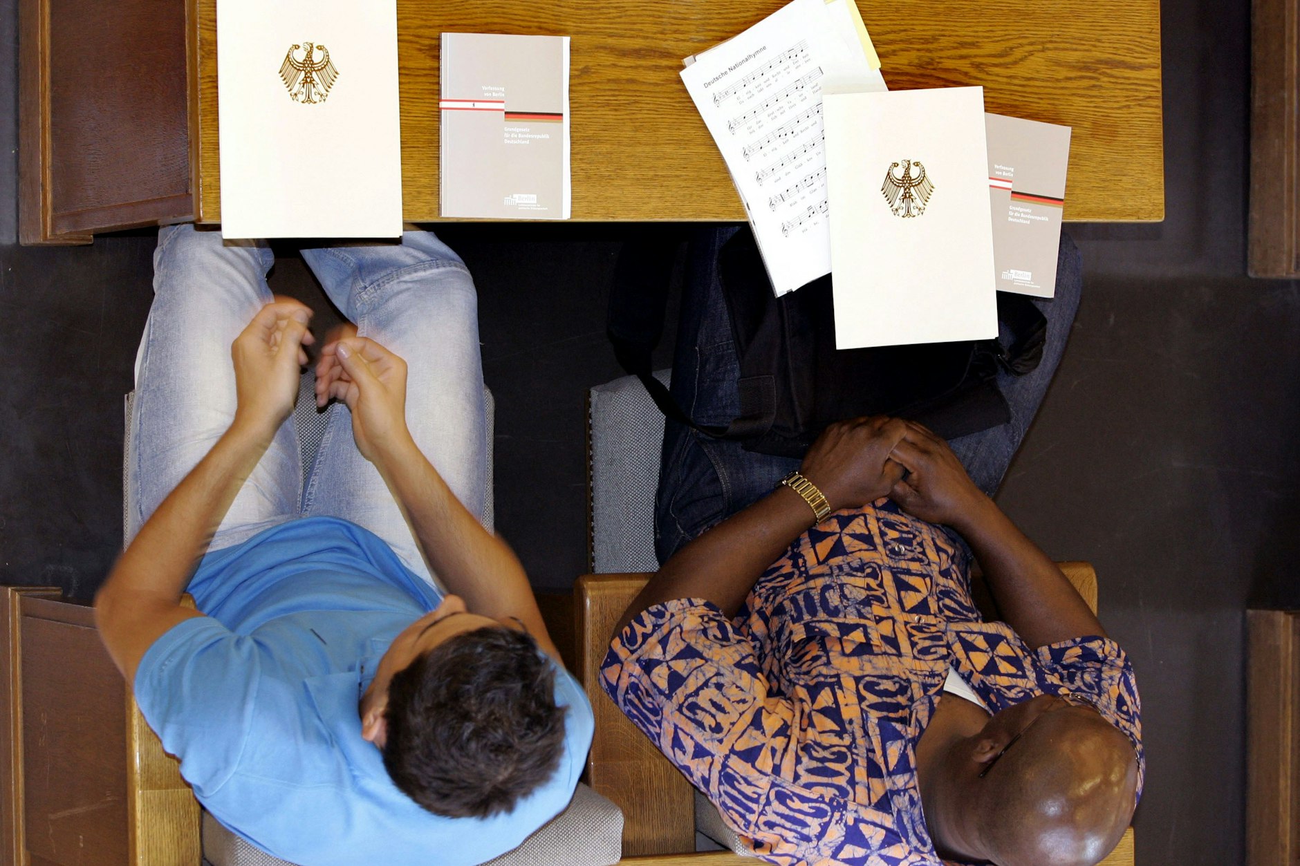 ARCHIV – Zwei Männer sitzen im Rathaus Neukölln, vor ihnen liegen ihre Einbürgerungsurkunden mit dem Bundesadler auf dem Tisch.