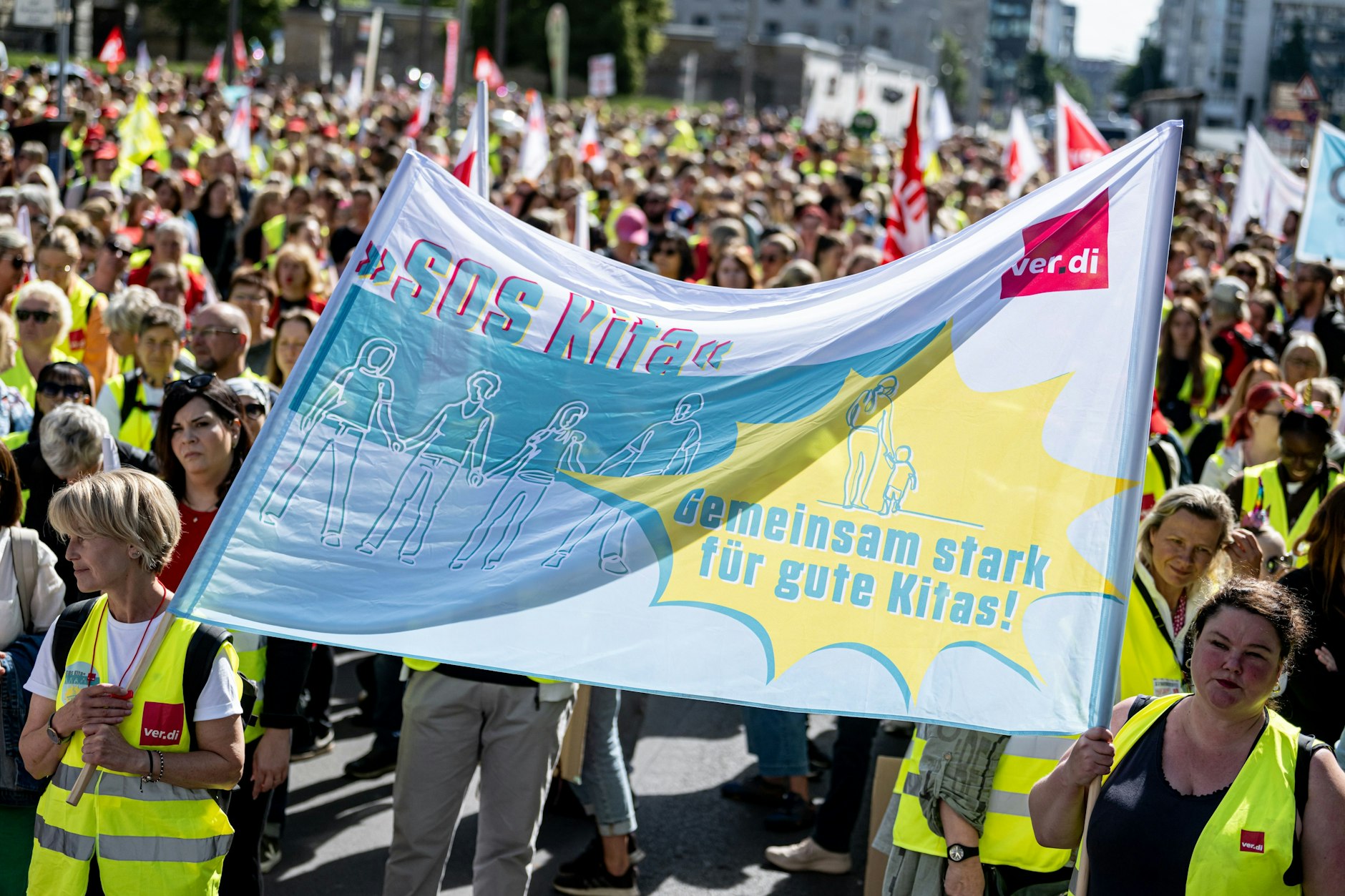 Personen stehen bei einem Warnstreik der Gewerkschaft verdi in kommunalen Kitas vor dem Abgeordnetenhaus mit einem Banner mit der Aufschrift „SOS Kita. Gemeinsam stark für gute Kitas!“. Verdi hat erneut zum Warnstreik an kommunalen Kitas aufgerufen. 