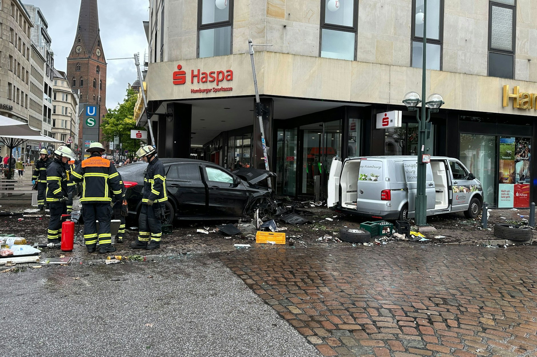 Helfer der Hamburger Feuerwehr stehen an dem demolierten Mercedes vor einer Sparkasse, daneben ist der silberfarbene Kleinbus zu sehen.