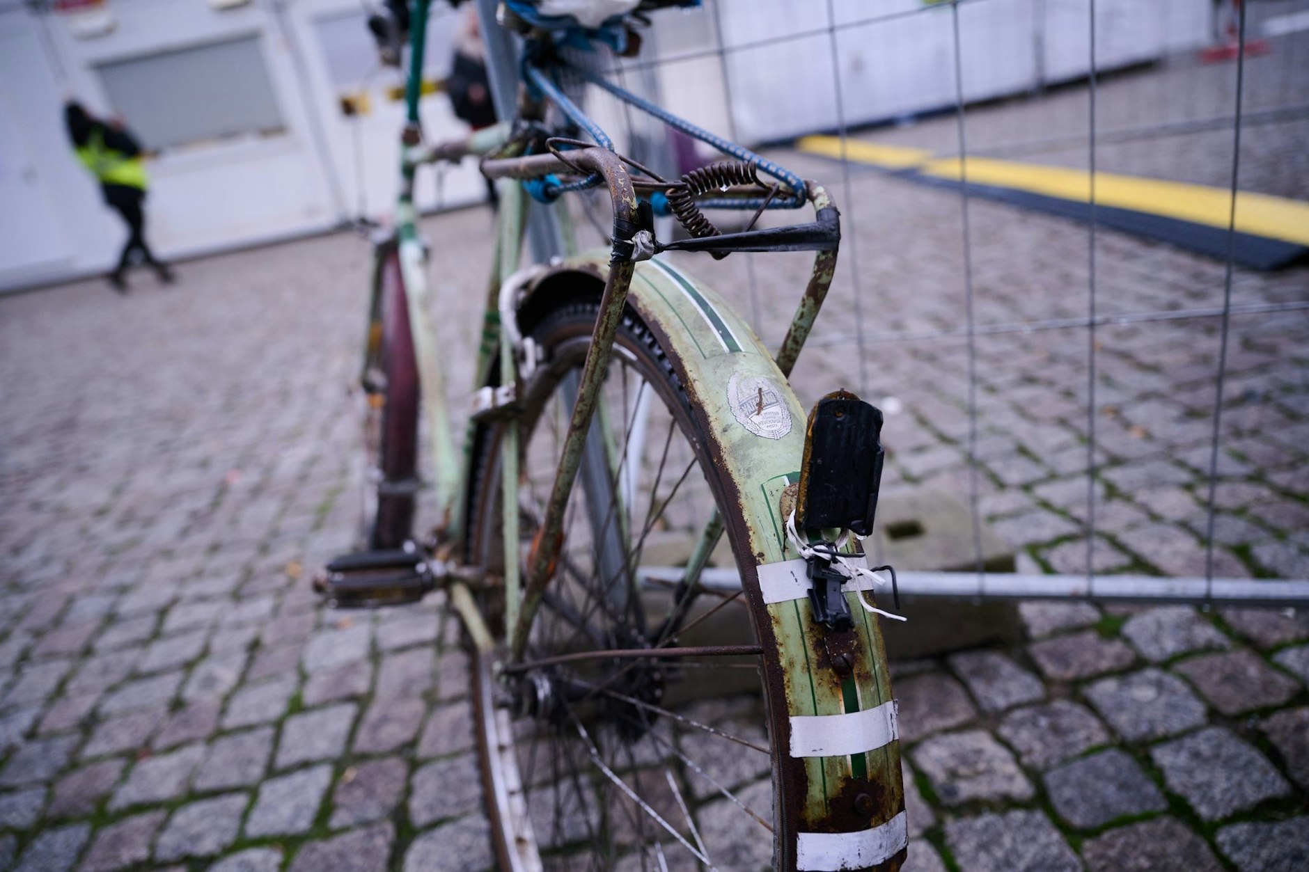Ein herrenloses Fahrrad steht an einem Bauzaun vor dem Hauptbahnhof, am Vorderrad wurde ein gelber Zettel des Ordnungsamtes befestigt. Auf dem Zettel steht der Hinweis, dass das Rad durch eine lange Standzeit aufgefallen ist, der Eigentümer wird aufgefordert, es wegzuräumen.