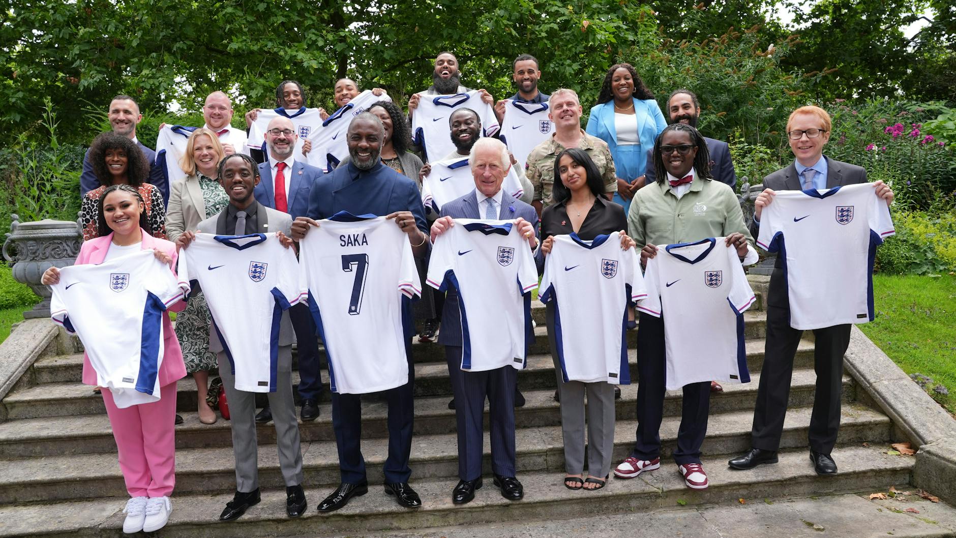 König Charles III. (Mitte) mit Idris Elba (Mitte links) und jungen Leuten, die Trikots der englischen Fußballmannschaft halten, während sie an einer Veranstaltung des King's Trust teilnehmen,