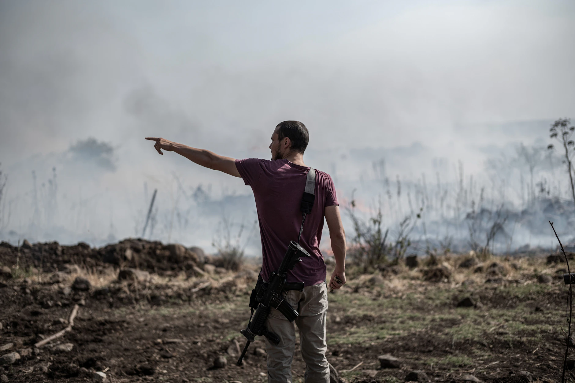 Ein bewaffneter Mann steht in der Nähe eines Feuers, das durch einen Raketen- und Drohnenangriff vom Libanon auf Israel verursacht wurde