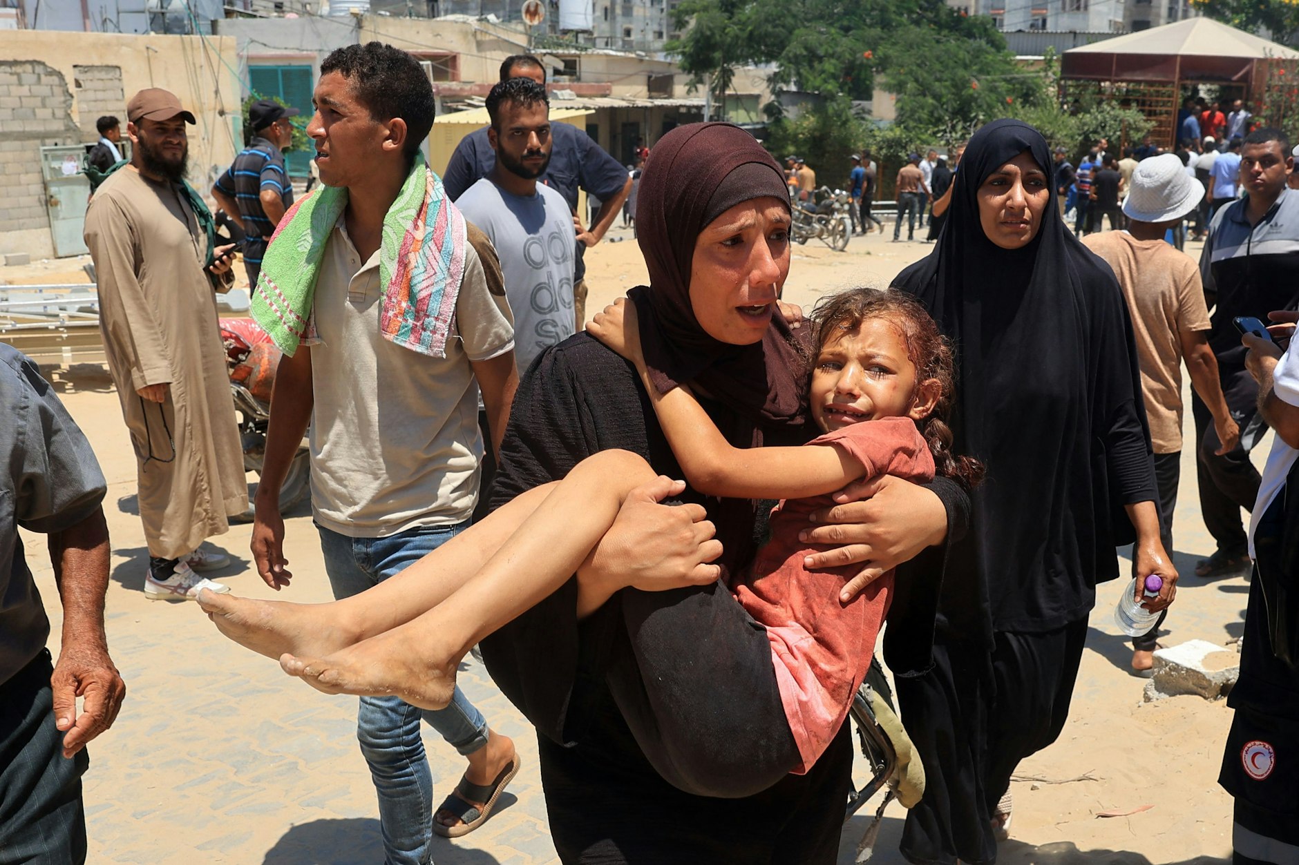 Eine palästinensische Frau trägt nach dem Angriff auf das Flüchtlingslager von Al-Mawasi ein verletztes Kind zu Rettungskräften. 