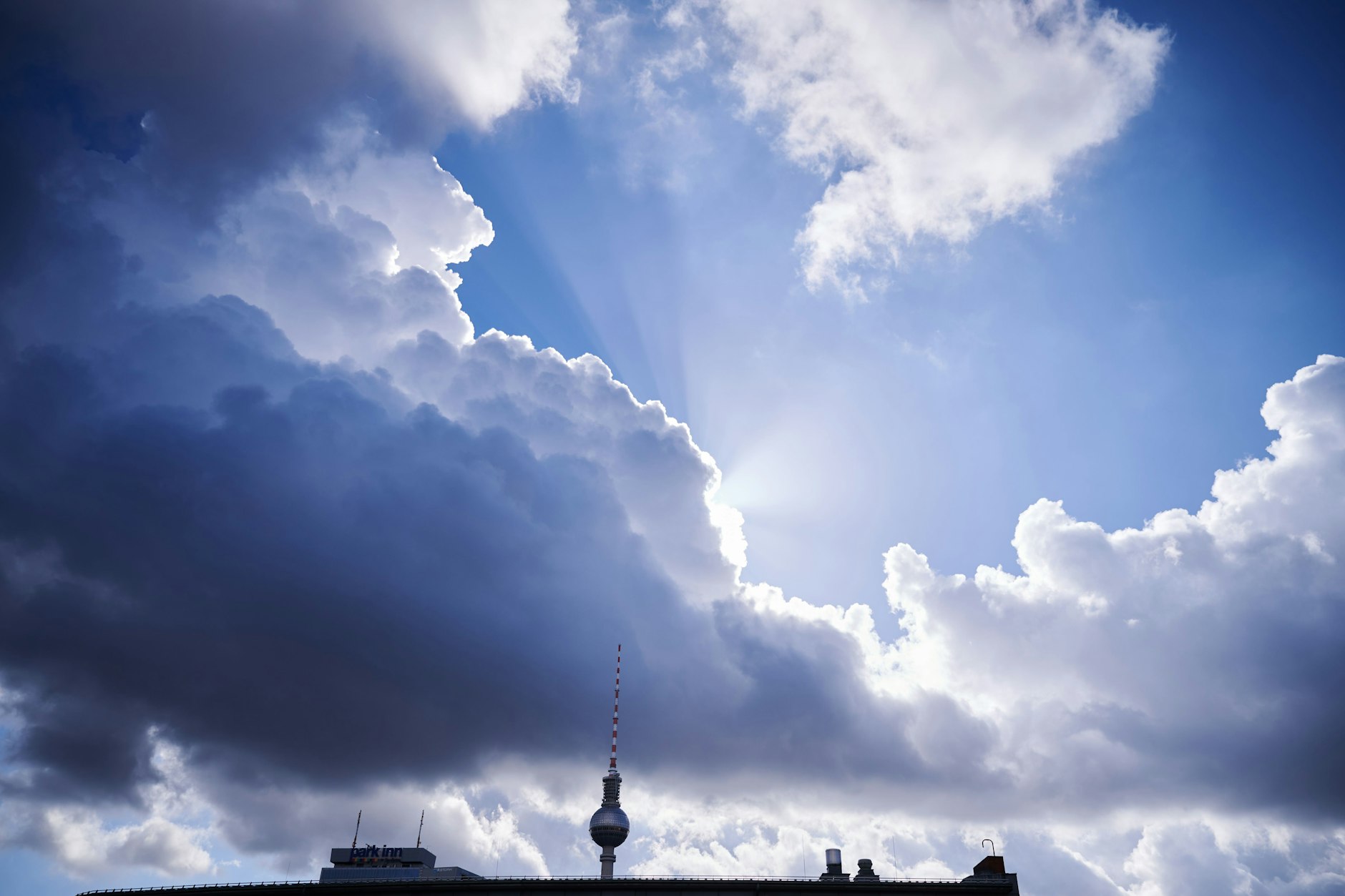 Sonnenstrahlen hinter einer dunklen Wolke über dem Fernsehturm am Alex.