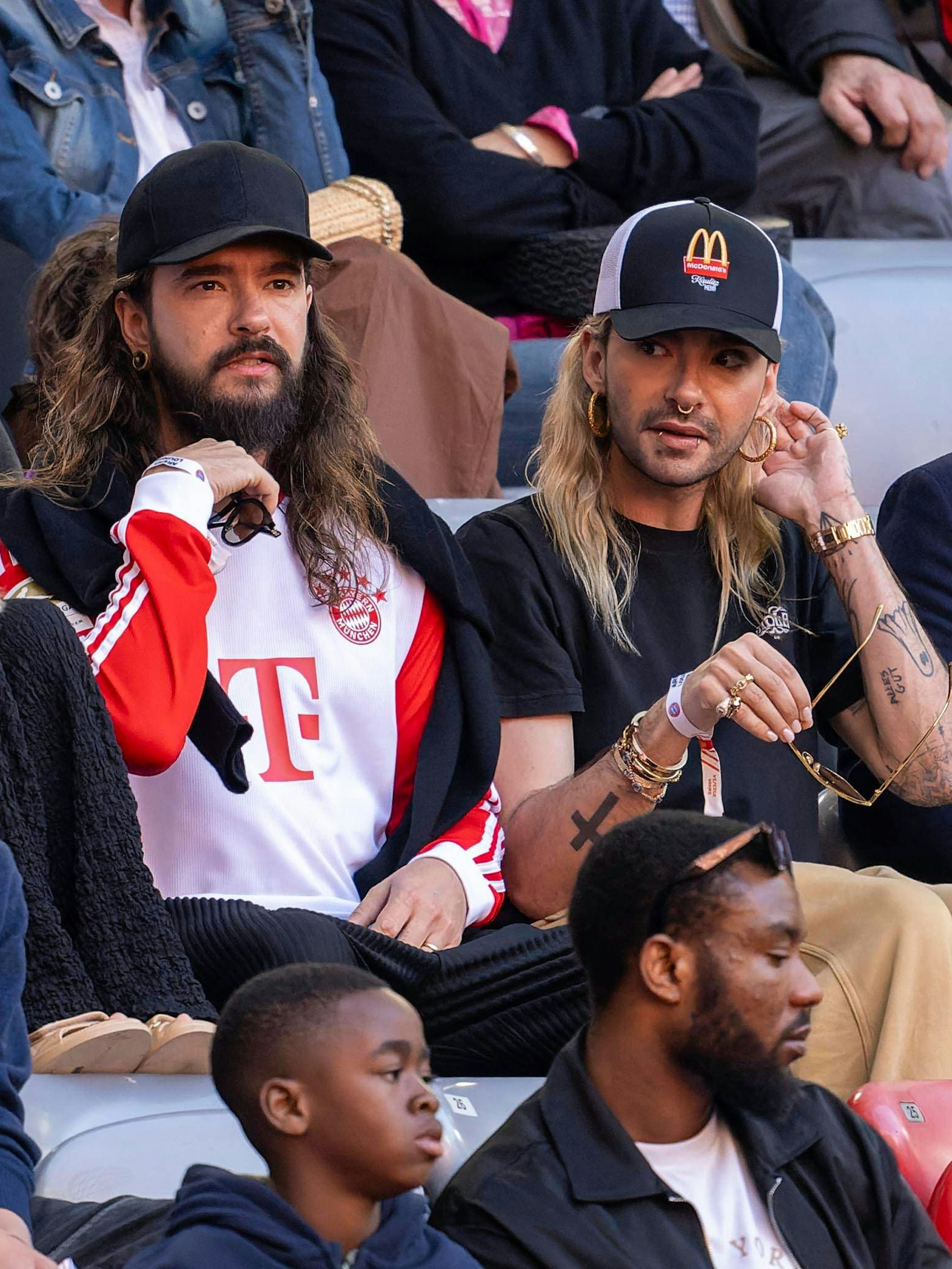 2024: Tom und Bill bei einem Fußballspiel in München. Privat trägt Bill gerne Basecaps und bedruckte T-Shirts, so wie Tom.