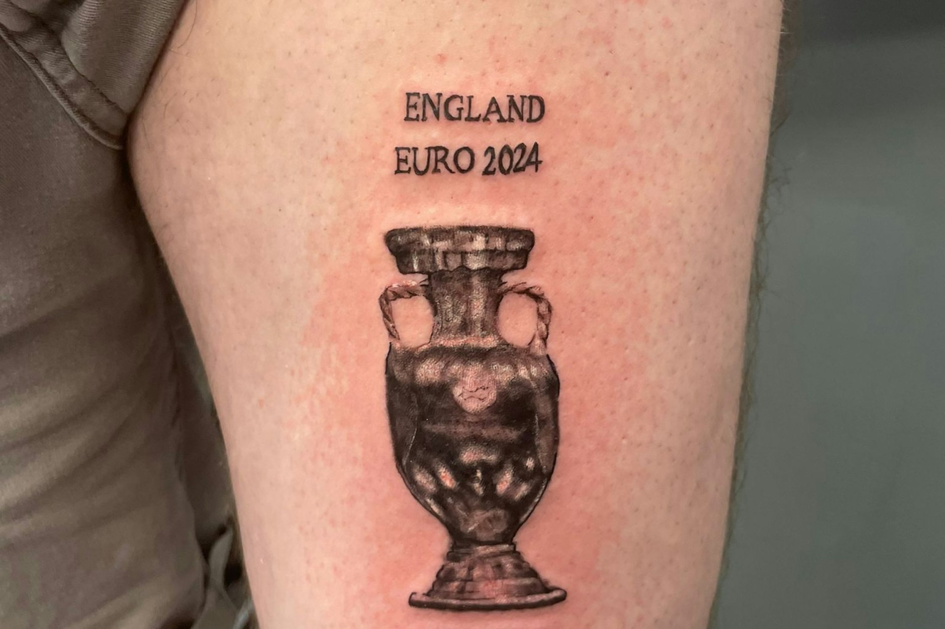 Fußballfan Dan Thomas zeigt seine Tätowierung, die eine Trophäe und die Worte «England Euro 2024 Winners» zeigt, vor dem Finale gegen Spanien am vergangenen Sonntag. Thomas hat nicht vor, es zu verdecken und sagt, dass er das Tattoo trotz der Niederlage «immer noch liebt». 
