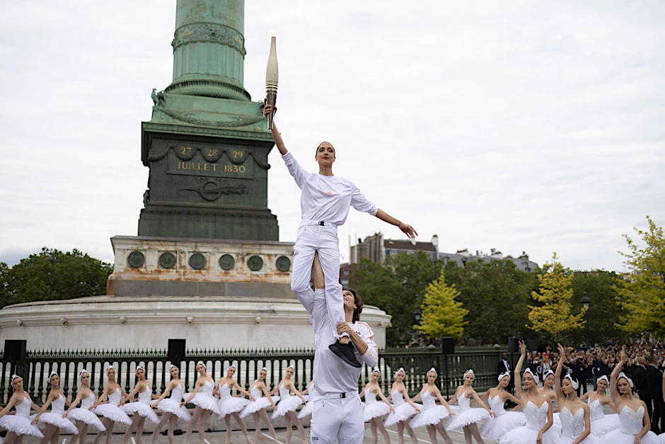Olympischer Fackellauf auf dem Place de la Bastille. Trägerin der Flamme Dorothee Gilbert, Solotänzerin des Balletts der Pariser Oper, und Hugo Marchand, französischer Balletttänzer, führen die olympische Fackel vor der Bastille-Oper am 14. Juli 2024 in Paris, Frankreich.