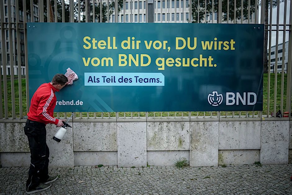 Ein Arbeiter säubert ein Plakat der neuen Imagekampagne des Bundesnachrichtendienstes (BND) mit der Aufschrift «Stell dir vor, du wirst vom BND gesucht» am Zaun der Zentrale des Dienstes.