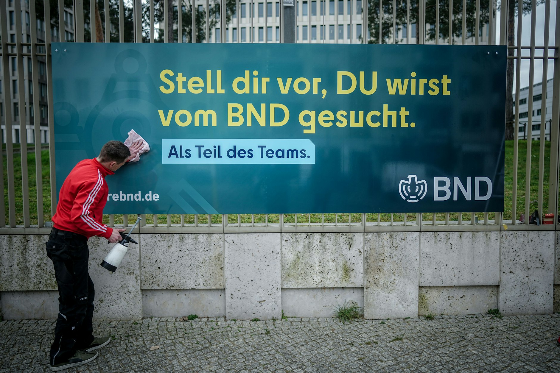 Ein Arbeiter säubert ein Plakat der neuen Imagekampagne des Bundesnachrichtendienstes (BND) mit der Aufschrift «Stell dir vor, du wirst vom BND gesucht» am Zaun der Zentrale des Dienstes.