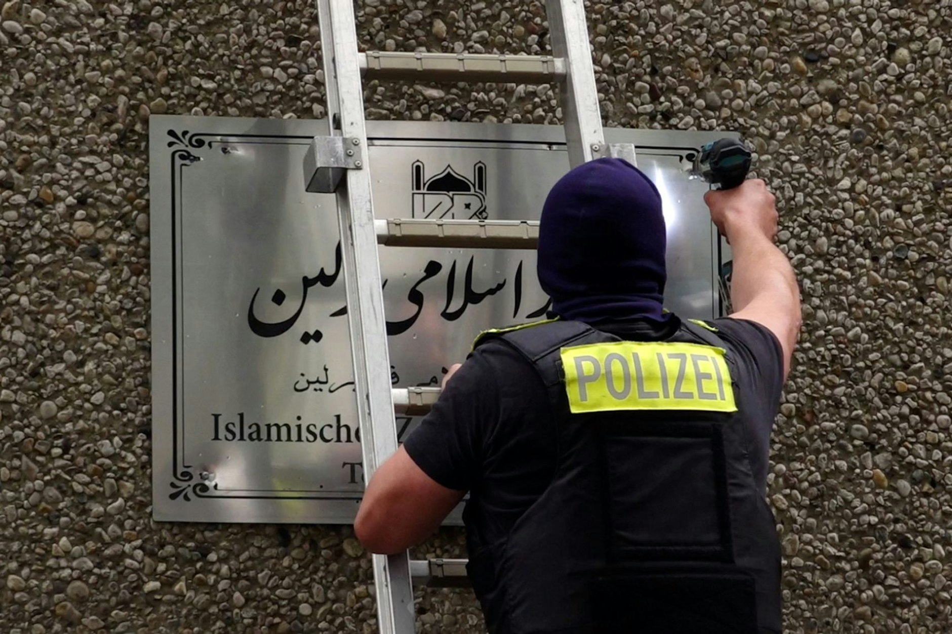 Ein Polizist entfernt ein Hinweisschild vom Islamischen Zentrum Berlin in der Ordensmeisterstraße. 
