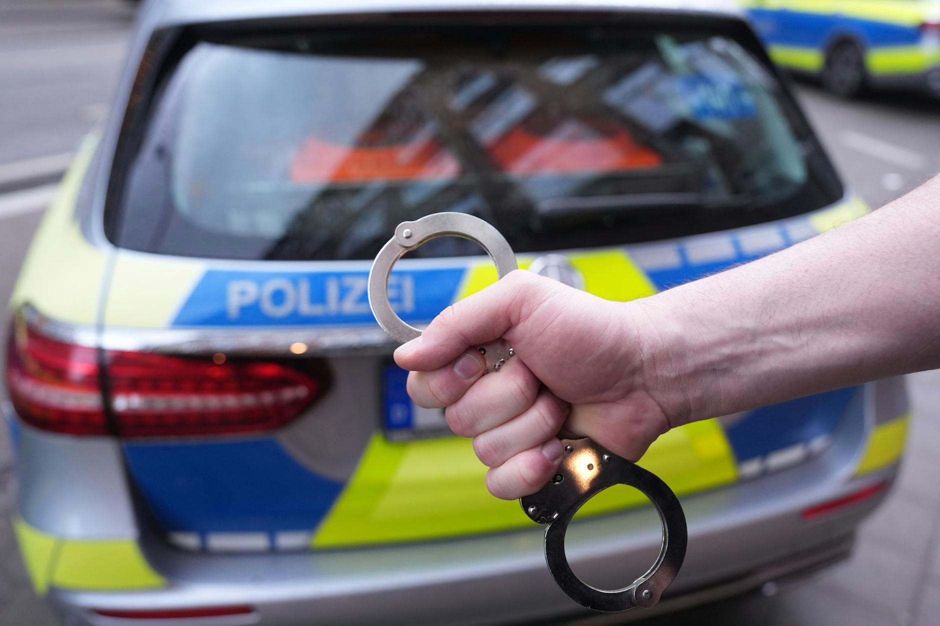 Ein Polizist hält Handschellen vor einem Einsatzfahrzeug in Hamburg hoch.