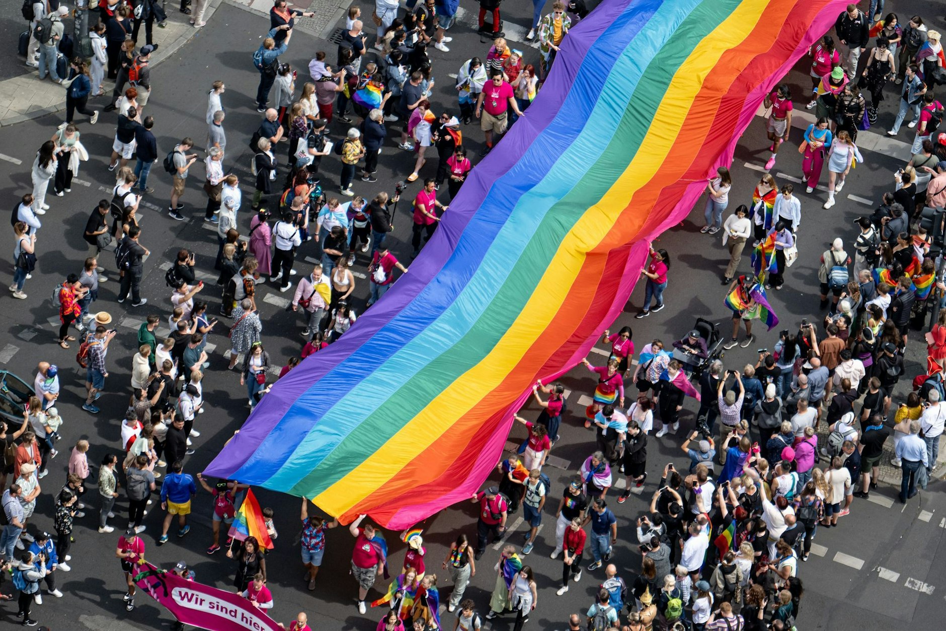 Menschen ziehen auf der 45. Berlin-Pride-Parade 2023 zum Christopher Street Day (CSD) mit einer überdimensionalen Regenbogenfahne durch die Stadt.