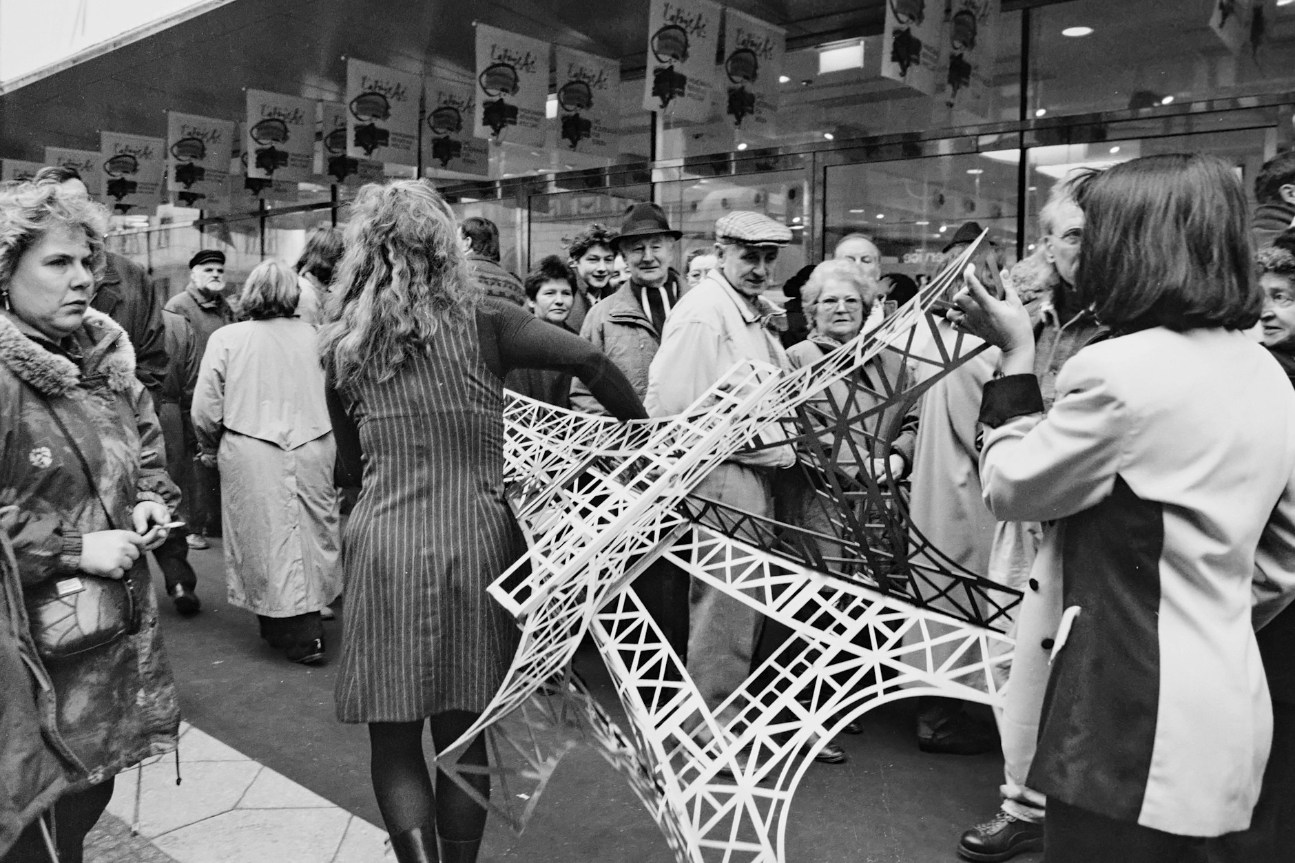 Mitarbeiterinnen tragen am 29. Februar 1996 zur Eröffnung ein Modell des Eiffelturms über den Gehweg, Hunderte Kunden stehen vor der Eröffnung Schlange.