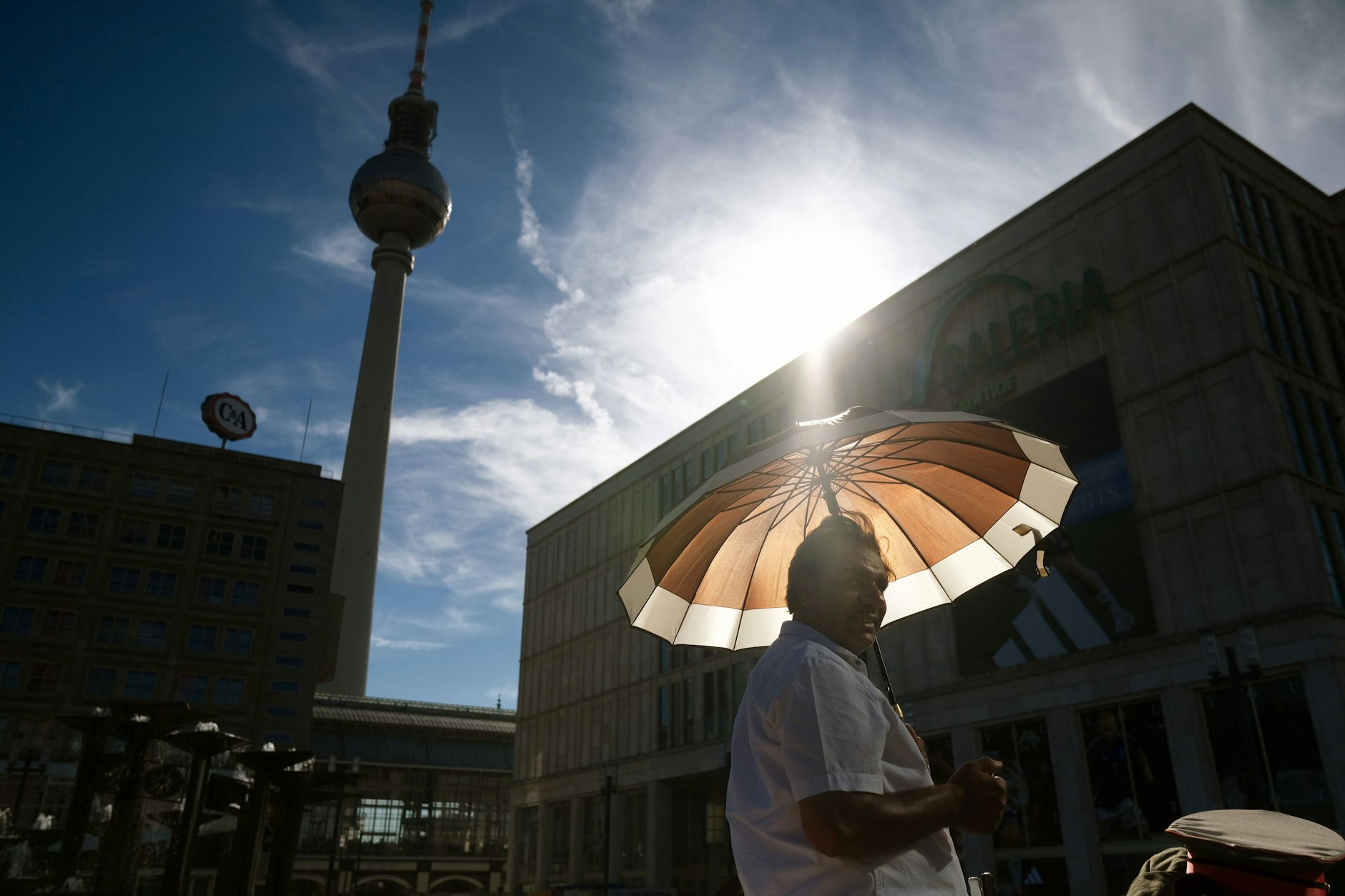 Ein Mann schützt sich am Alexanderplatz mit einem Schirm vor der Sonne.&nbsp;