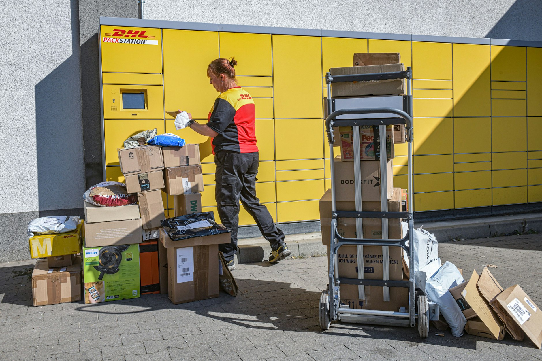Eine Paketbotin von DHL liefert Pakete an eine Packstation in Berlin aus. Der Job ist gefährlich.